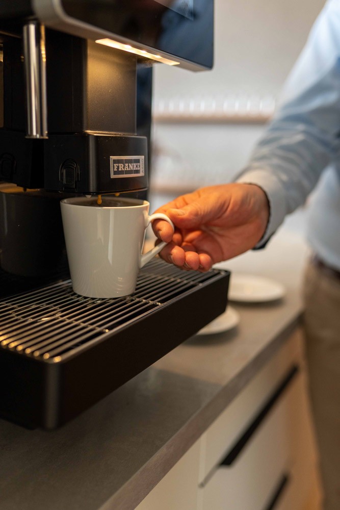 Hand einer Person stellt ihre Kaffeetasse unter den Kaffeevollautomaten.