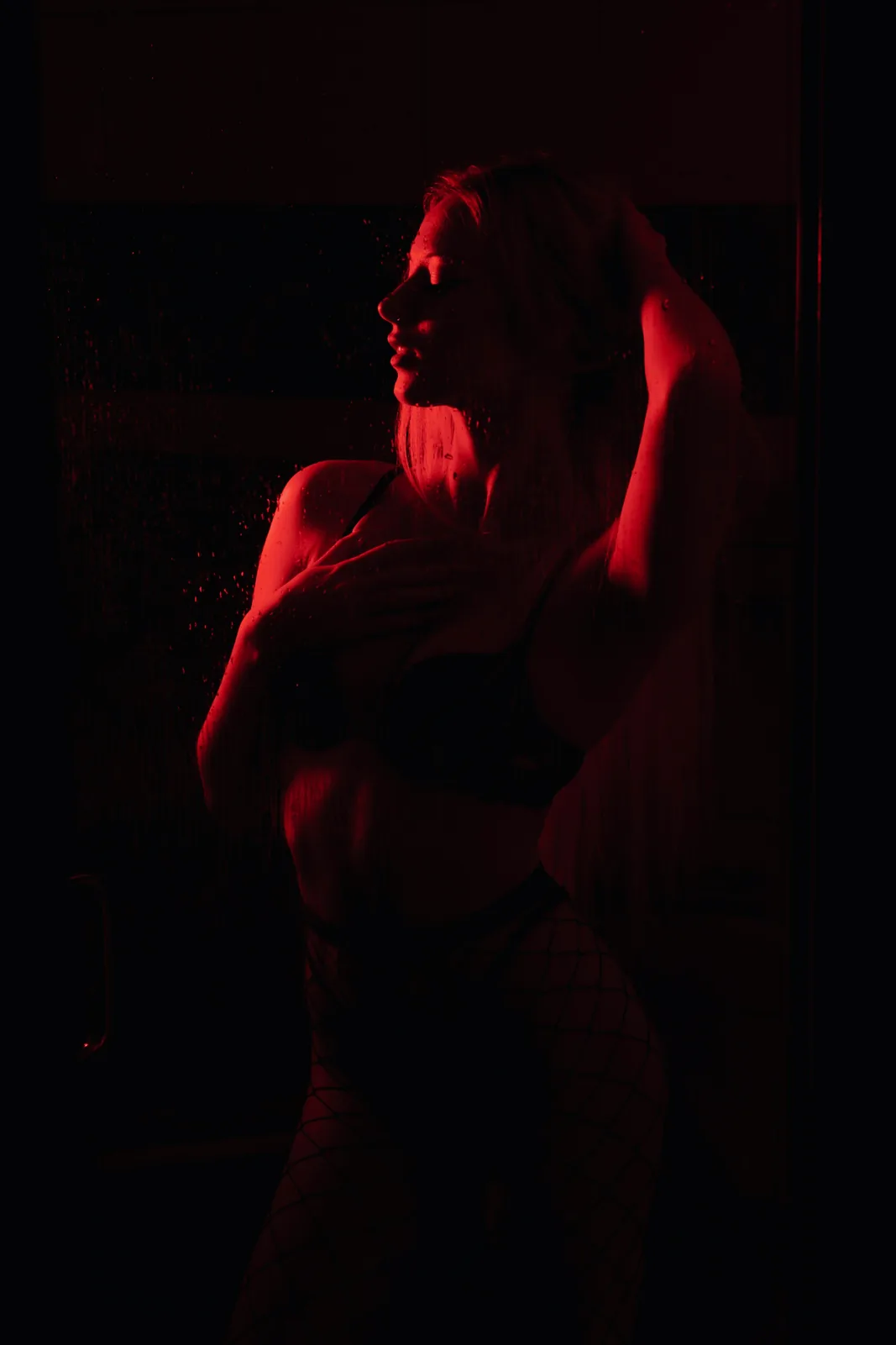 A woman bathed in red light in a dark infrared sauna