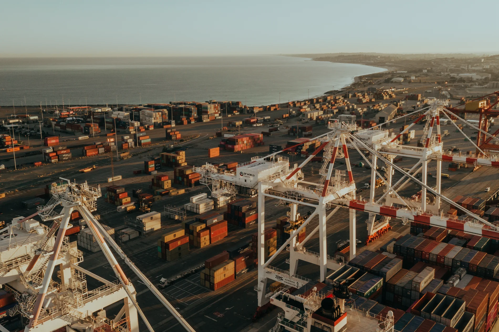 Aerial of a container terminal, white gantry cranes above stacked containers beside the sea