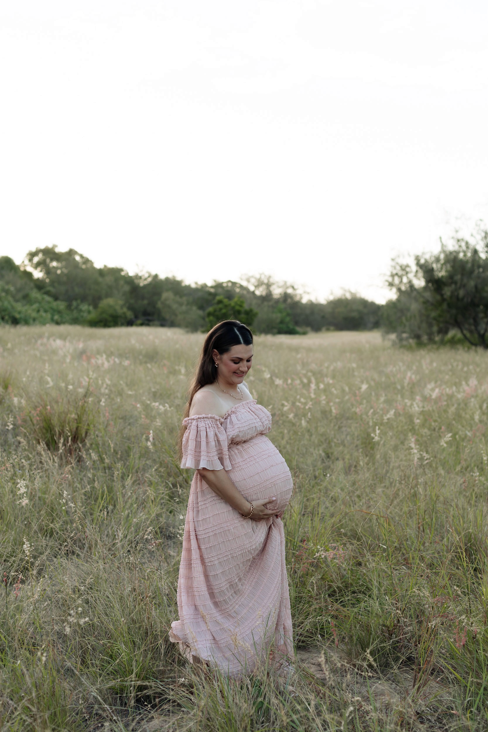 Solo maternity portrait in tall grassy field at sunset with expectant mother in soft flowy gown
