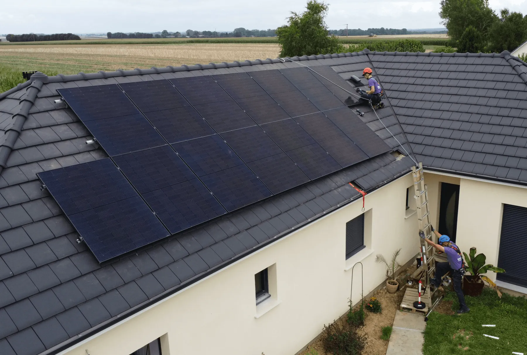 Photo d’un technicien Solarock qui pose devant une maison qui est équipée de panneaux solaires. Il vient d’effectuer une visite de contrôle dans le cadre de l’extension de garantie biennale proposée par Solarock.