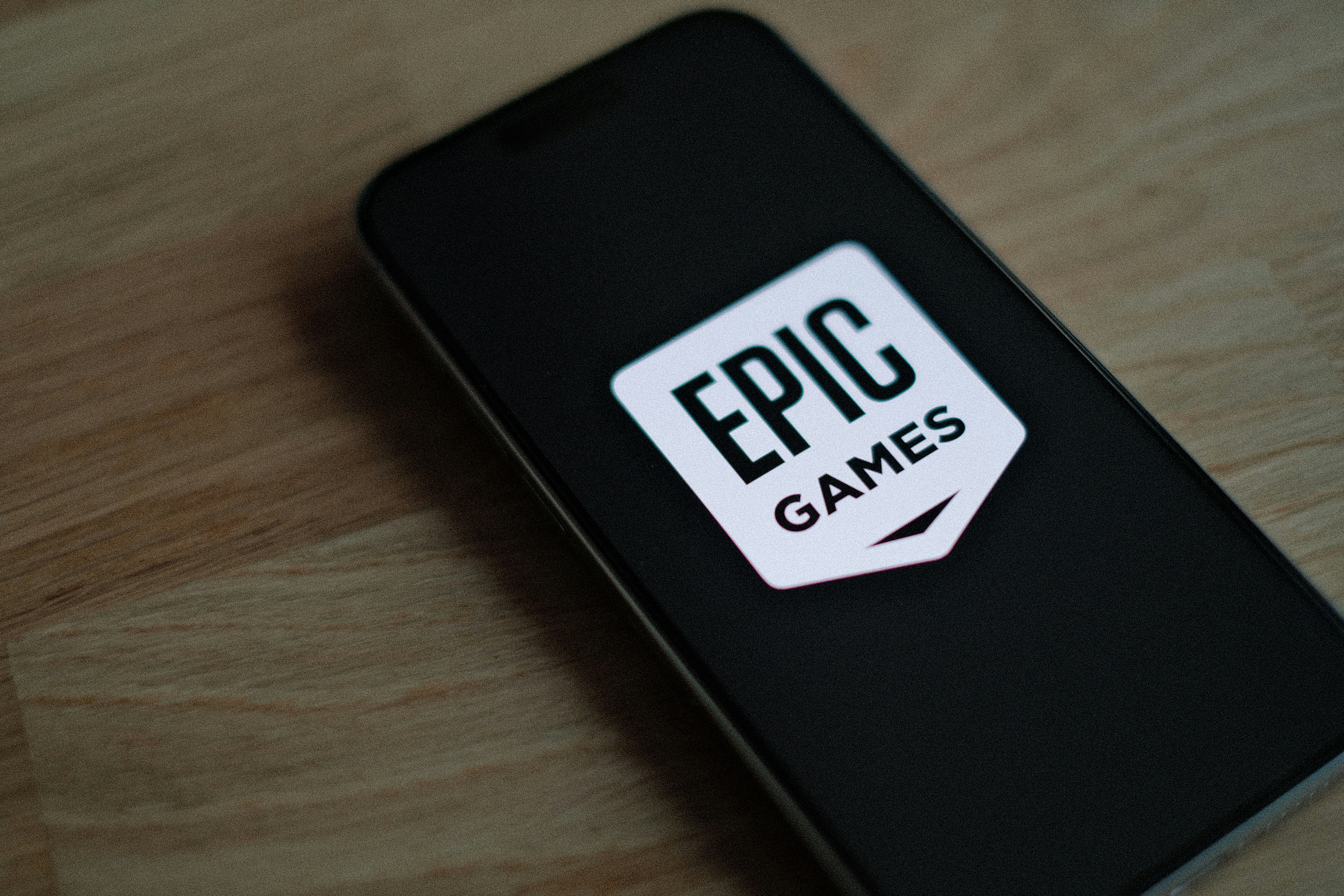 Smartphone lying on a wooden surface displaying the Epic Games logo on a dark screen