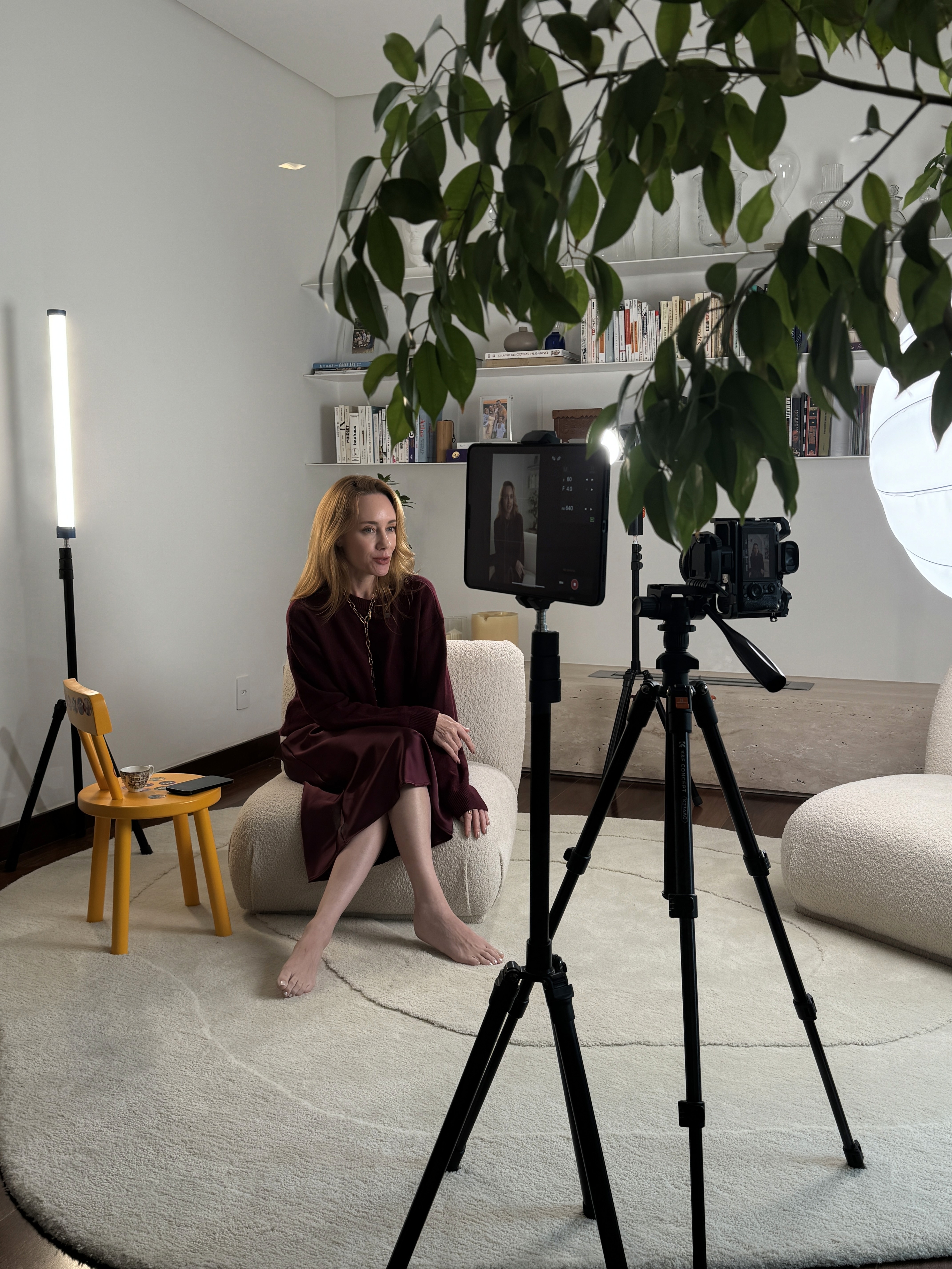 A smiling woman with her arms crossed, standing against a dark green background. She has long, dark hair.