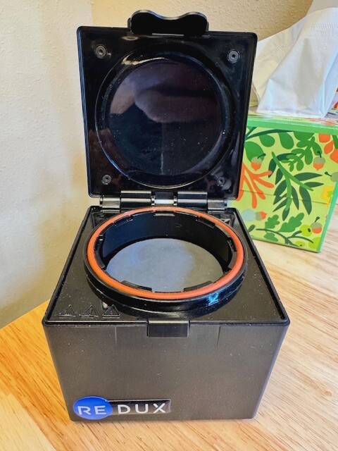 A black box with a circular light ring inside, partially opened, on a wooden surface with colorful background items.