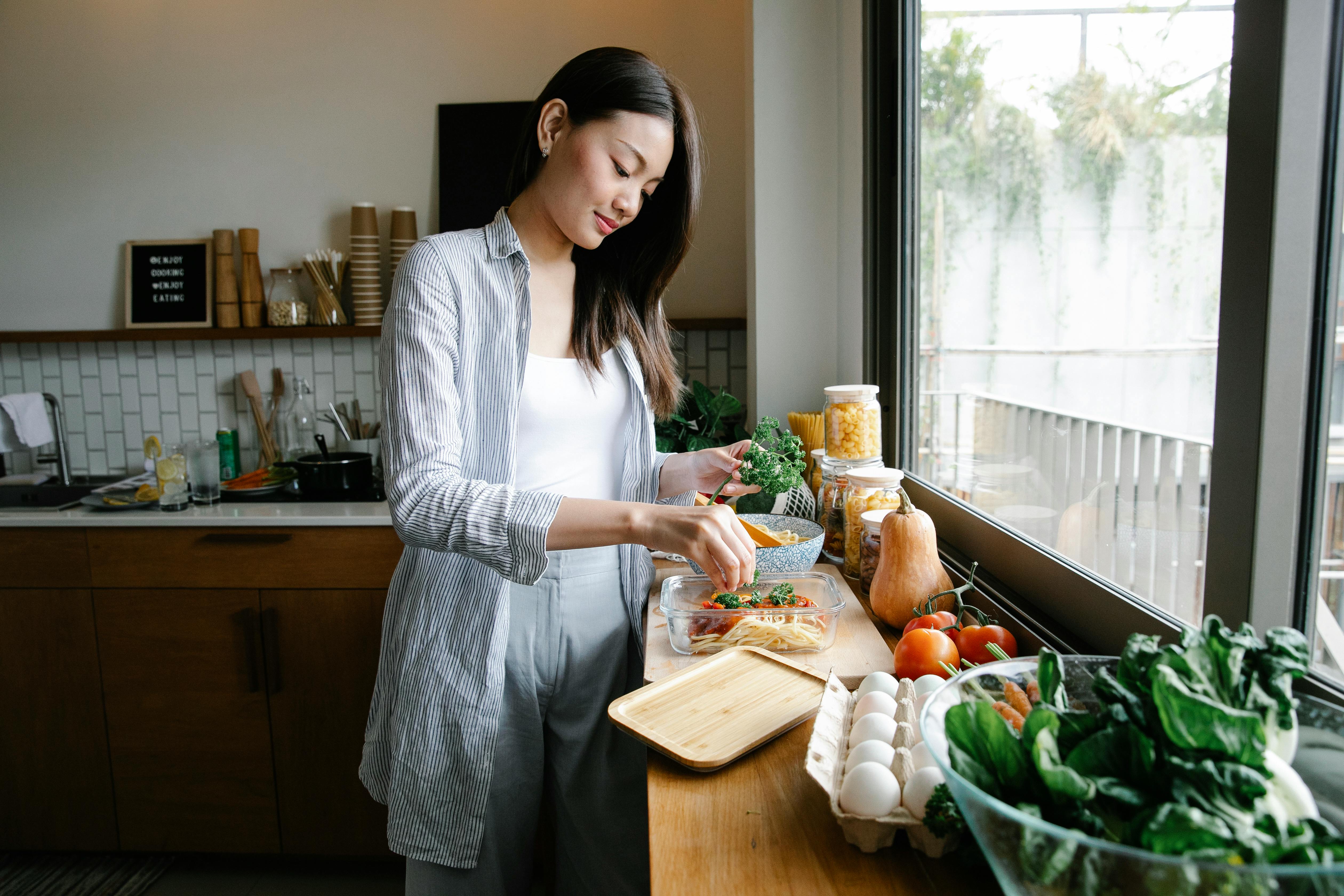 A newcomer to Canada preparing a fresh, pre-packaged meal kit in her apartment kitchen to save time and avoid grocery shopping during her first week of settlement.