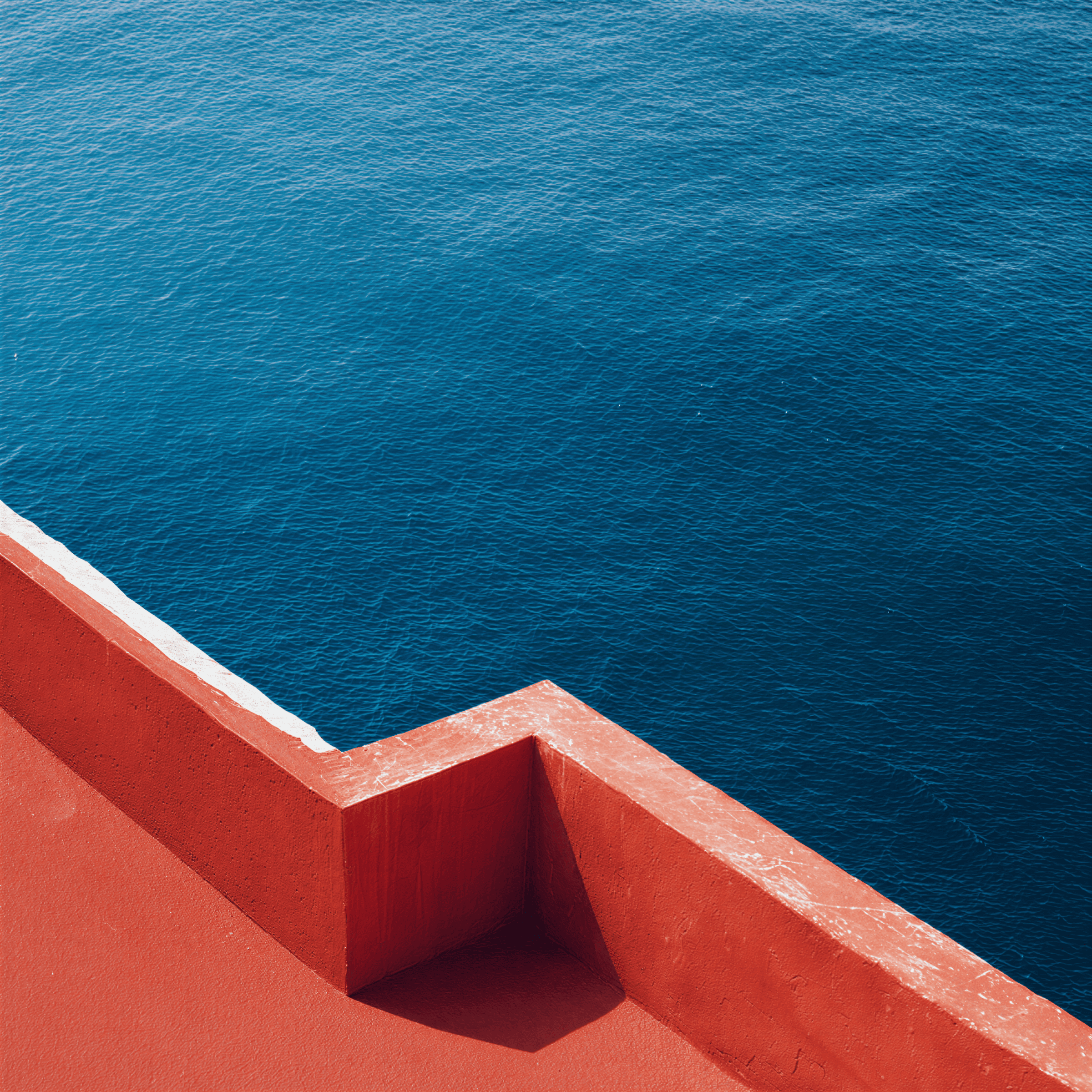 Red concrete corner against blue ocean water.