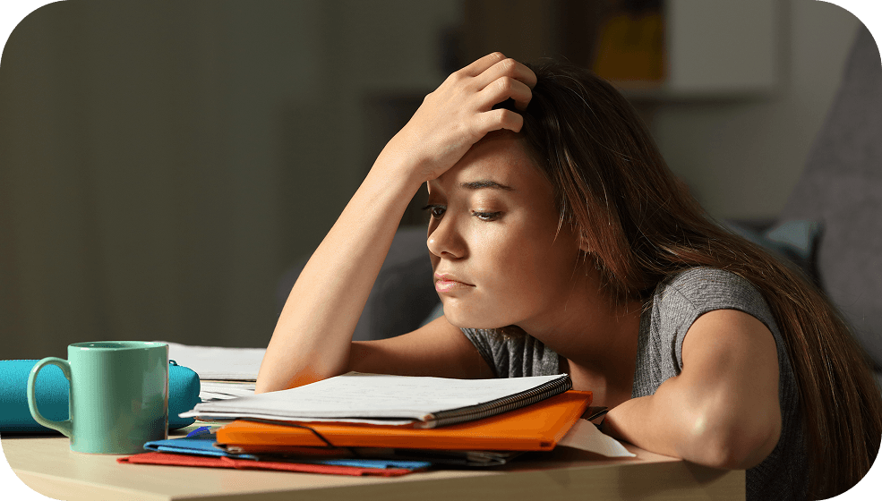 Student sitting at a desk looking overwhelmed with papers and folders, illustrating mental clutter