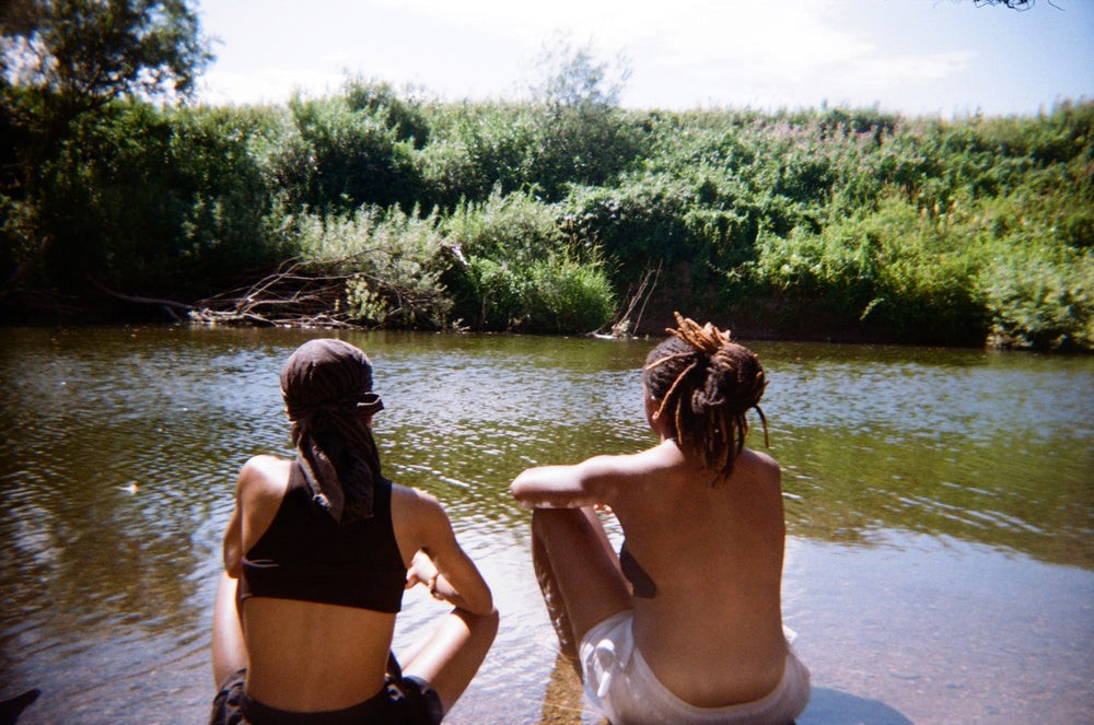 Two people sit on the river bank in the water whilst the sun is shining