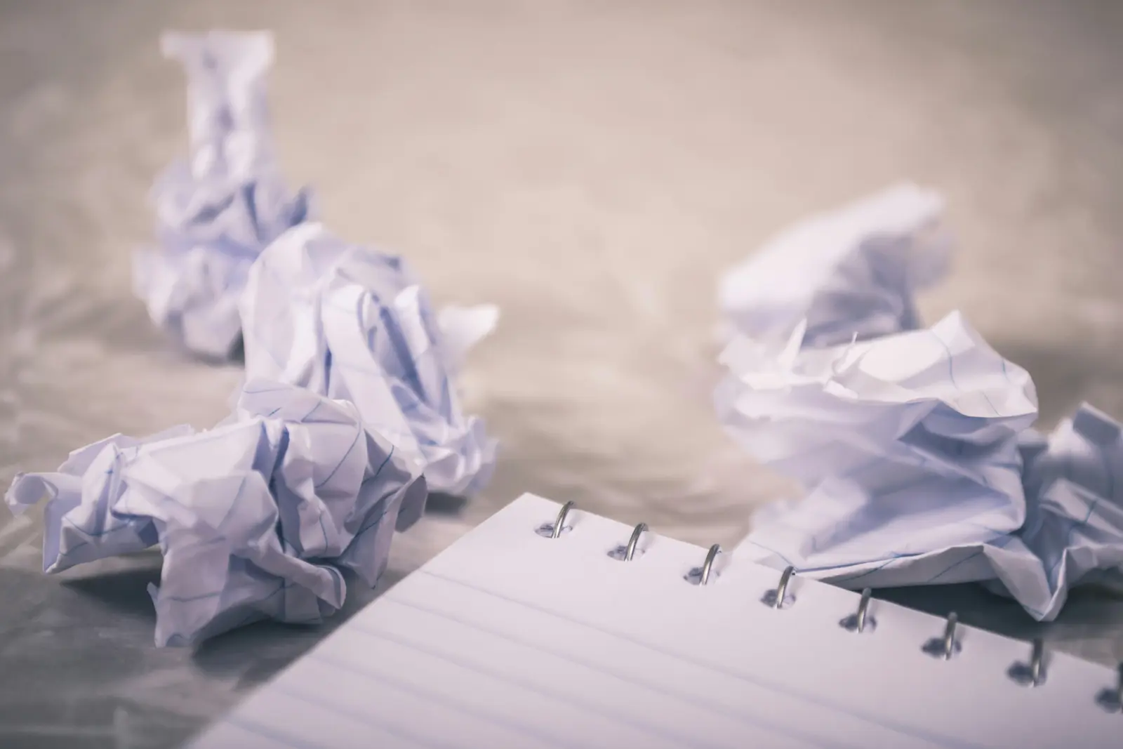 Crumpled paper balls on a desk next to an open notebook.