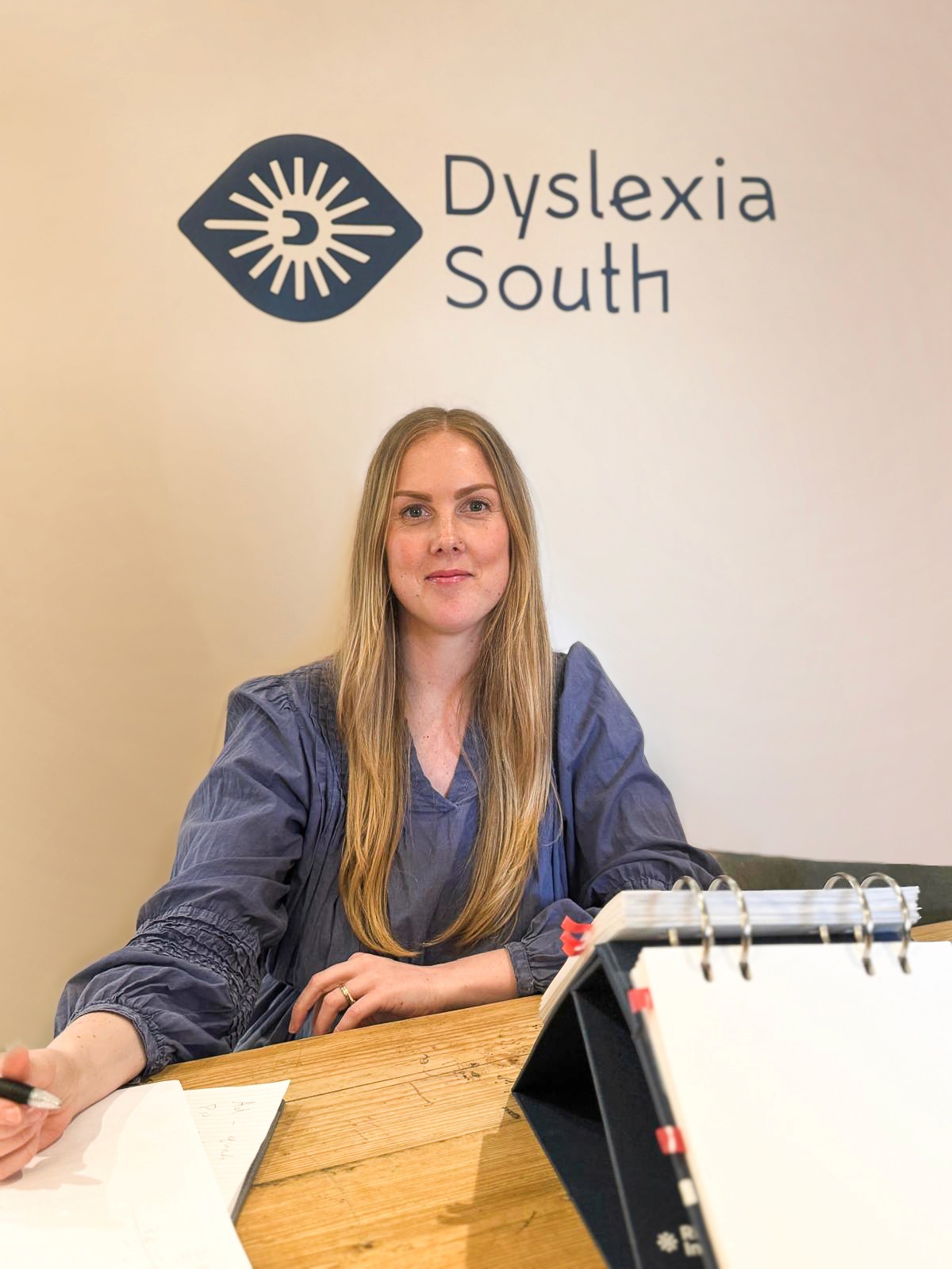 Dana sat at her desk with the dyslexia south logo behind her.