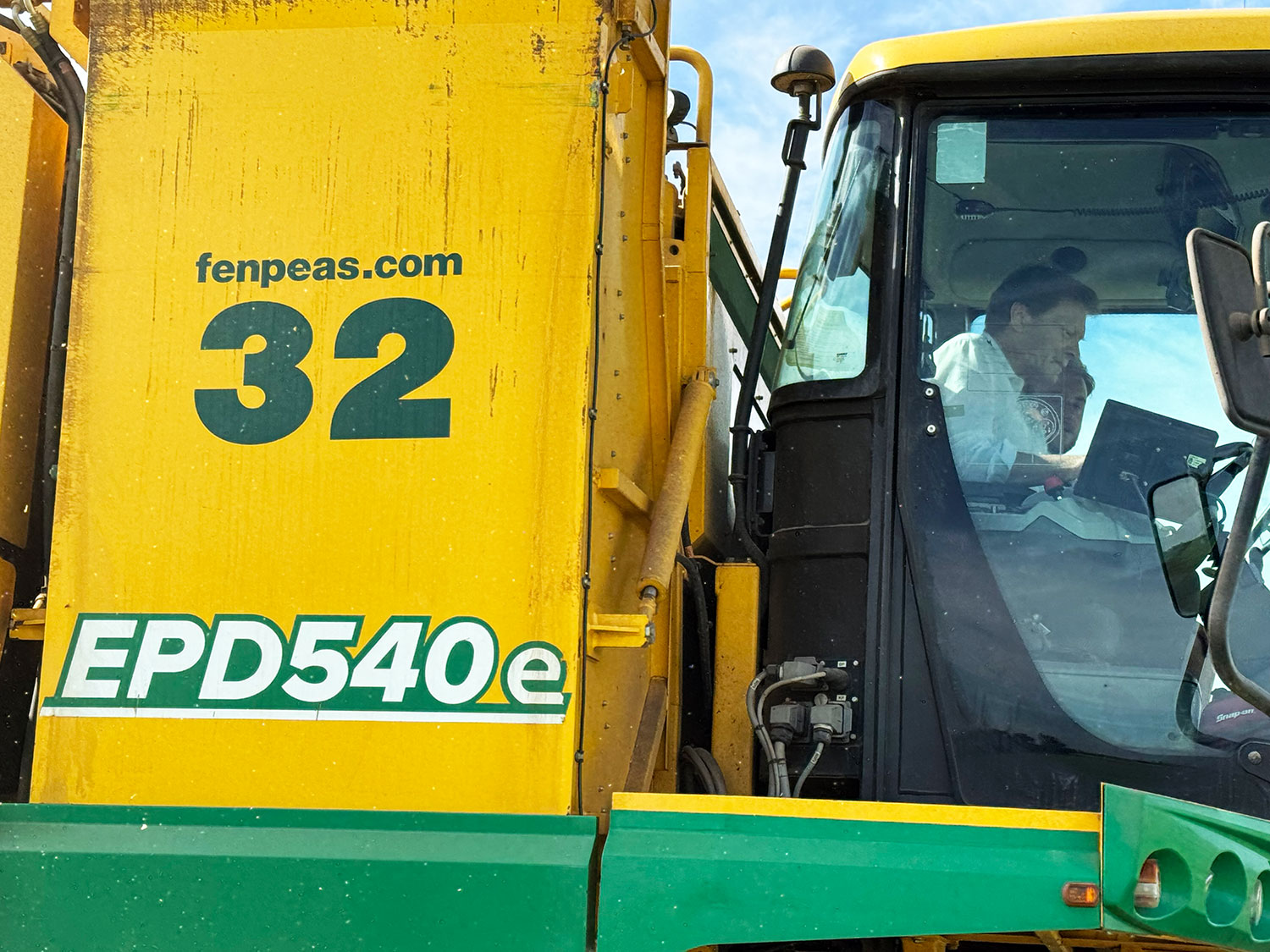 Richard Tice MP is sitting in the cab of a Ploeger viner and is being given a tour by a Fen Peas team member