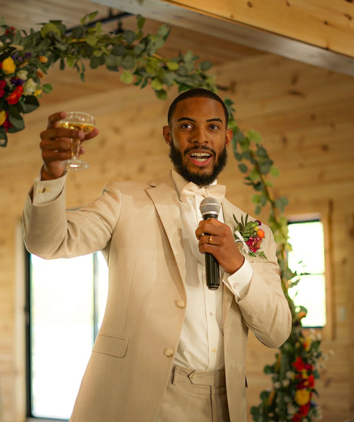 A bride in a lace wedding dress holds a vibrant bouquet of red and orange flowers.