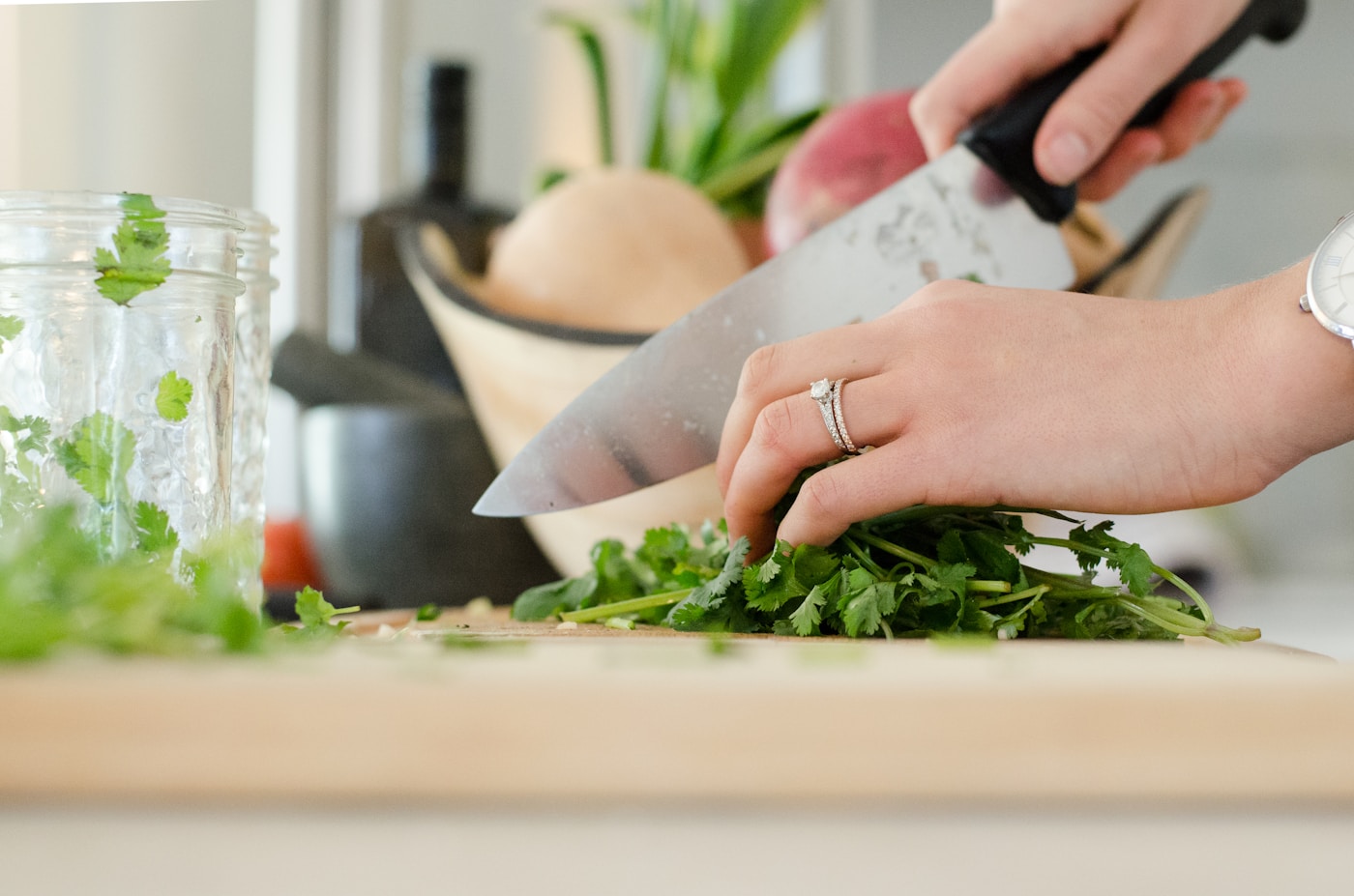 A person chopping fresh herbs and vegetables on a cutting board, preparing a nutritious meal at home