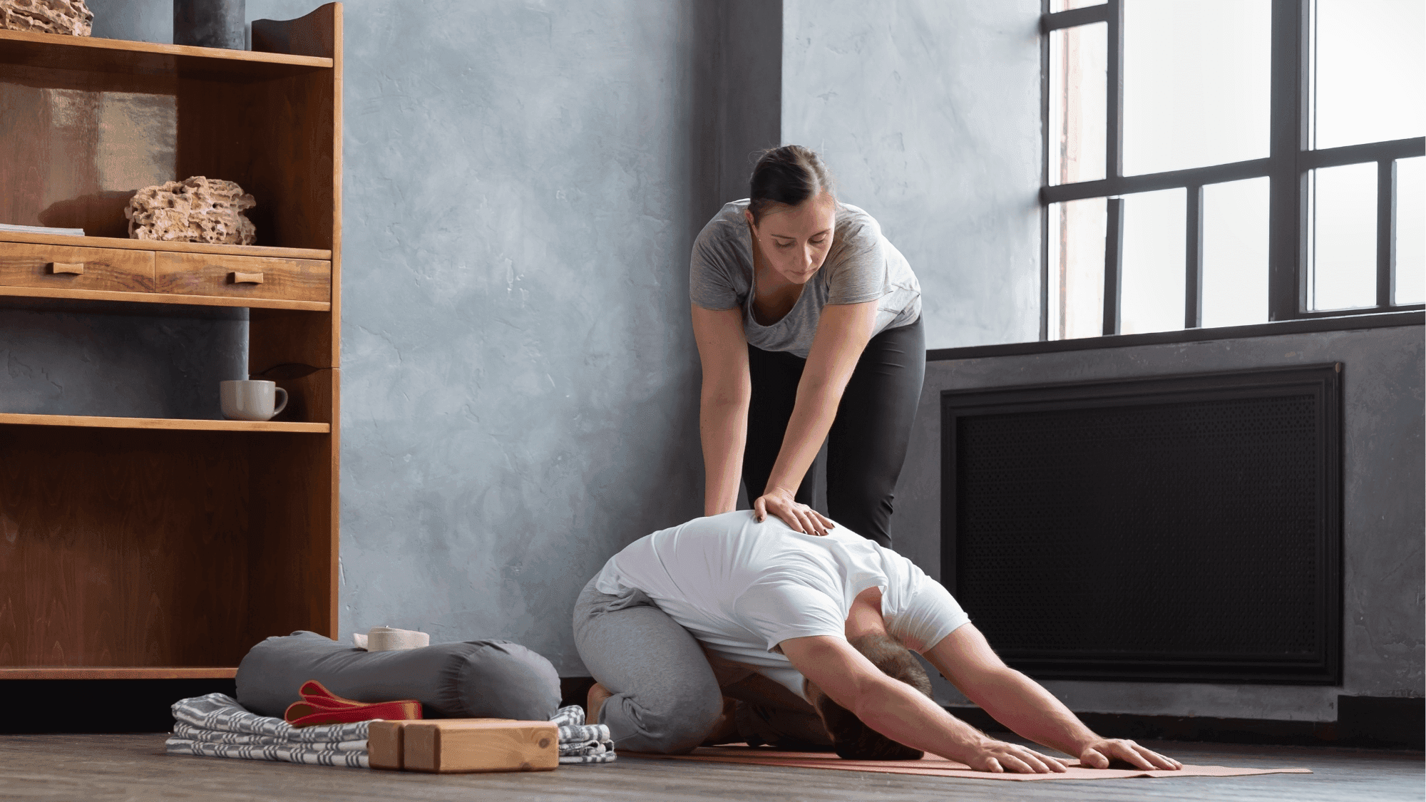 A new yoga teacher giving a modification to her student in childs pose.