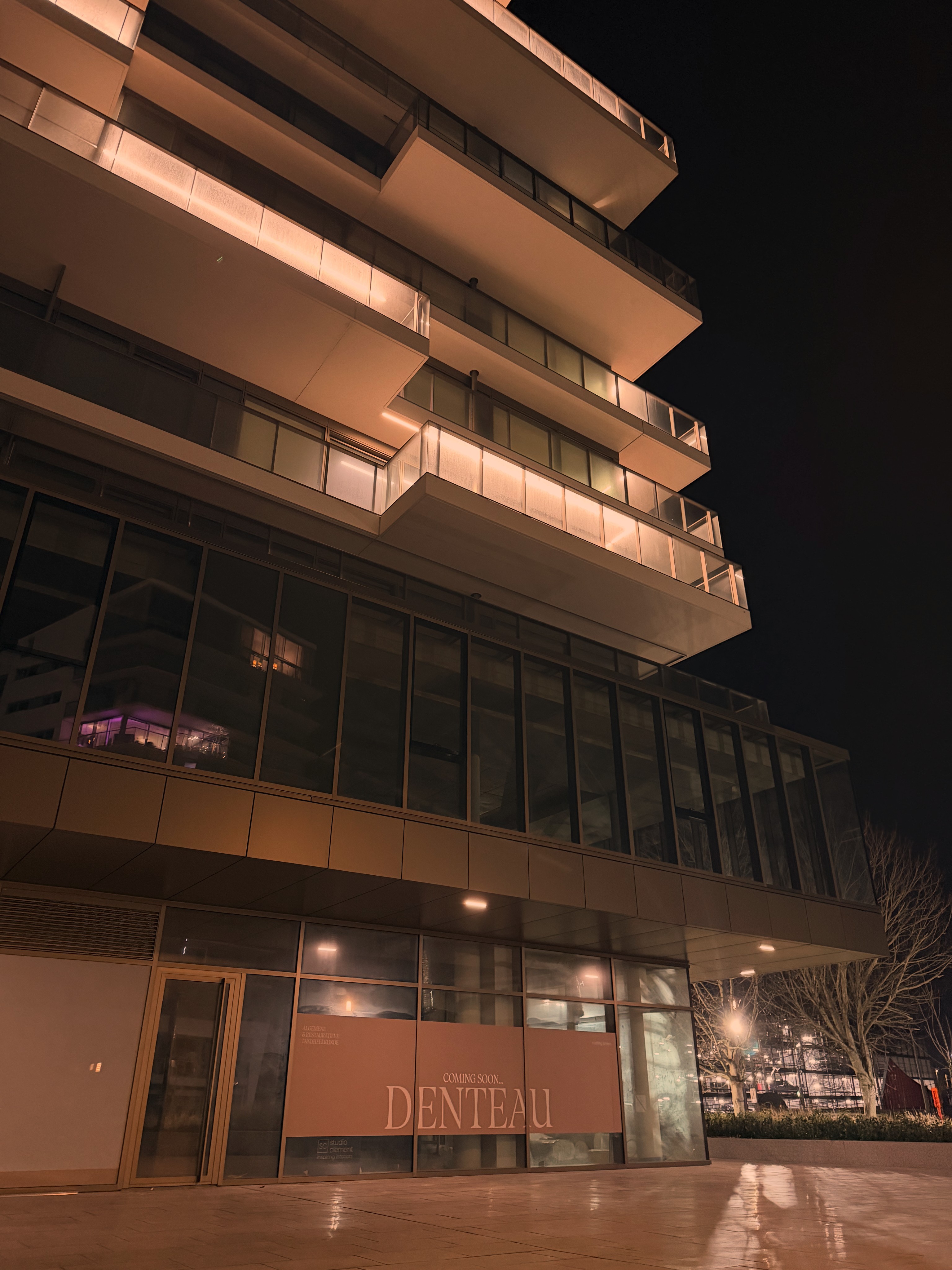 Close-up portrait of a young woman with green eyes, natural makeup, and dark hair, gently touching her face, against a neutral beige background