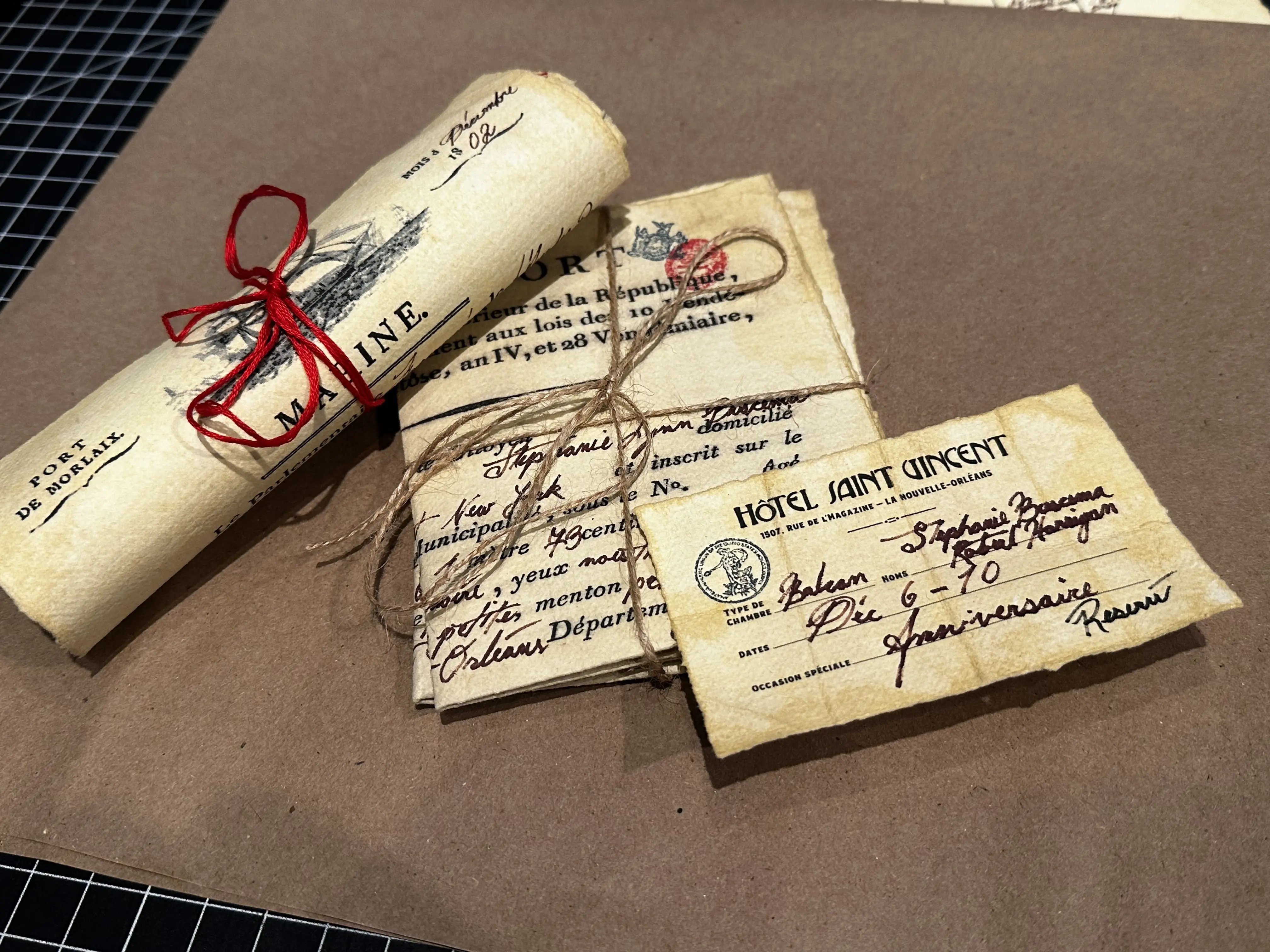 Vintage-style scrolls and postcards tied with twine and red ribbon are laid on a brown surface, showcasing Rob Harrigan's design aesthetic with a focus on nostalgic, antique elements.