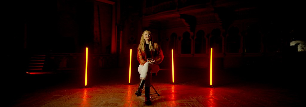 Person sitting on a stool in front of neon lights in a warehouse