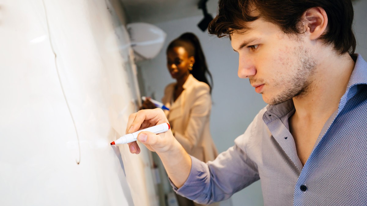 Two workshop facilitators writing with whiteboard markers on a whiteboard