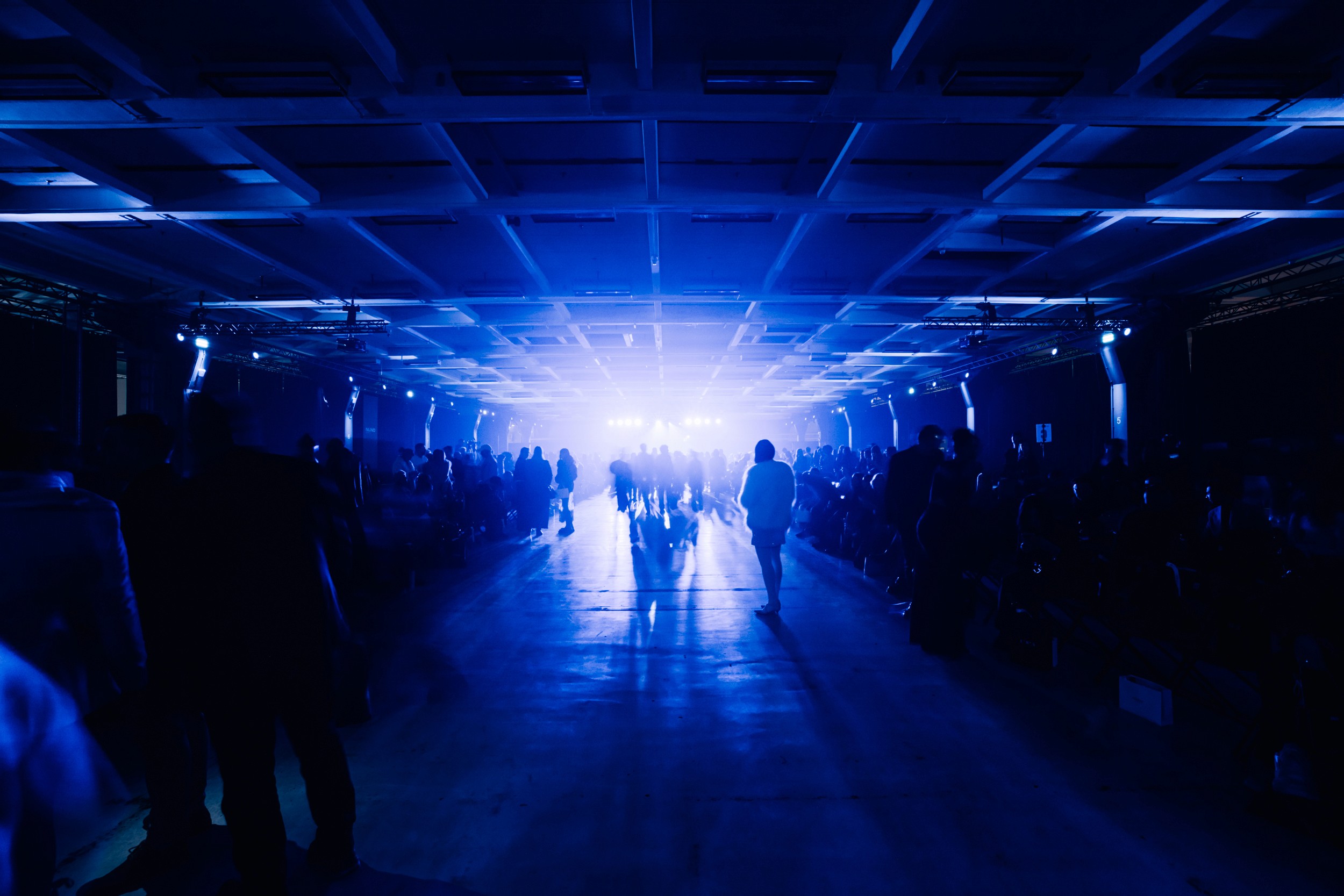 This image shows a large open event location, bathed in blue light, with guests walking around the space.