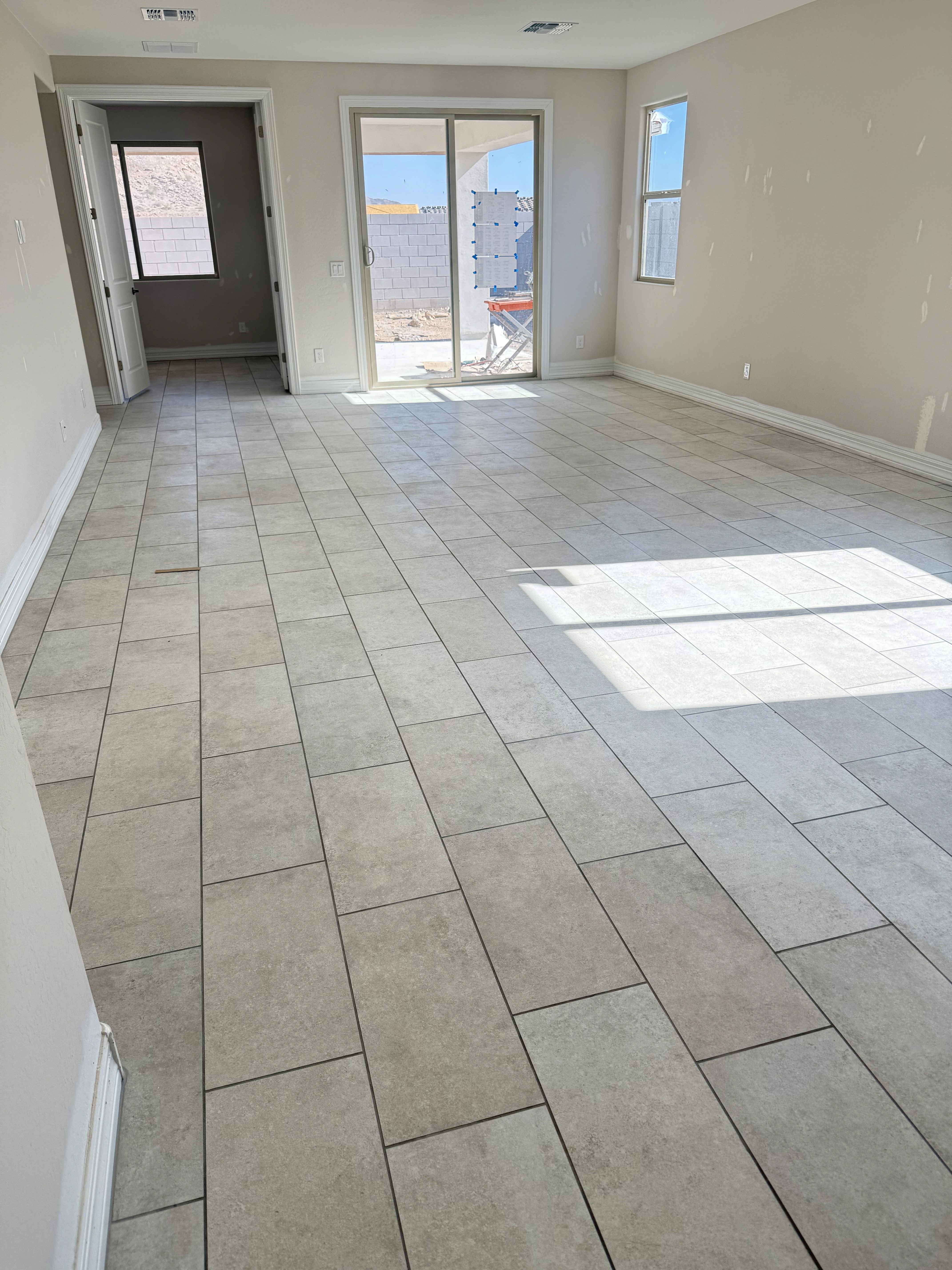 Modern living area with gray wood-look tile flooring, large sliding glass doors, and open space in a new home under construction.