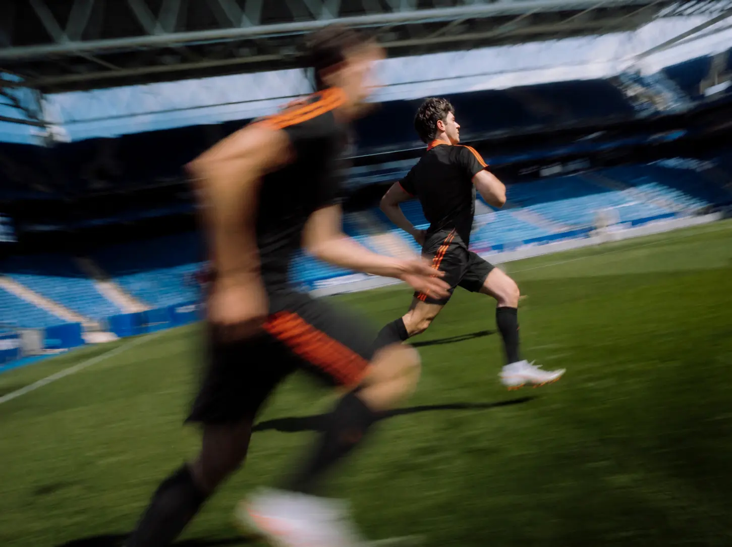 Two football players sprinting on a stadium pitch