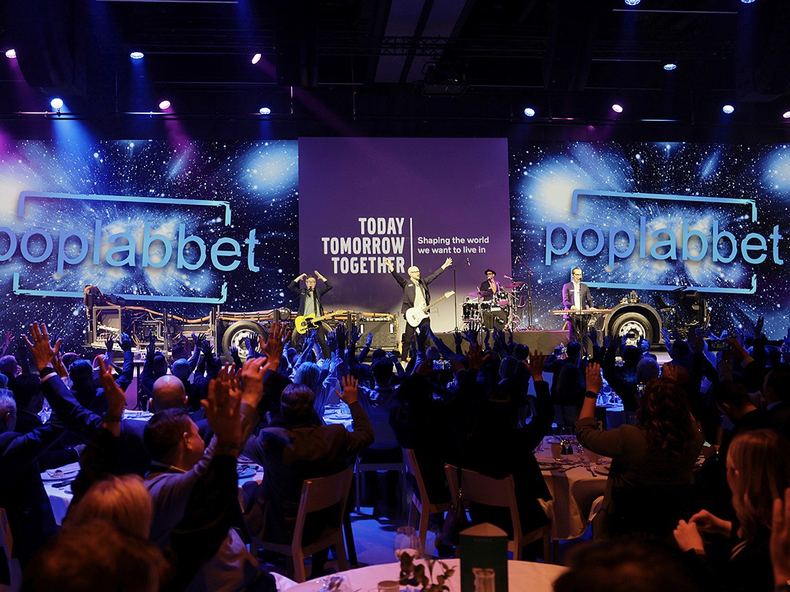 Ett band som spelar på en scen inför en publik som sträcker händerna i luften