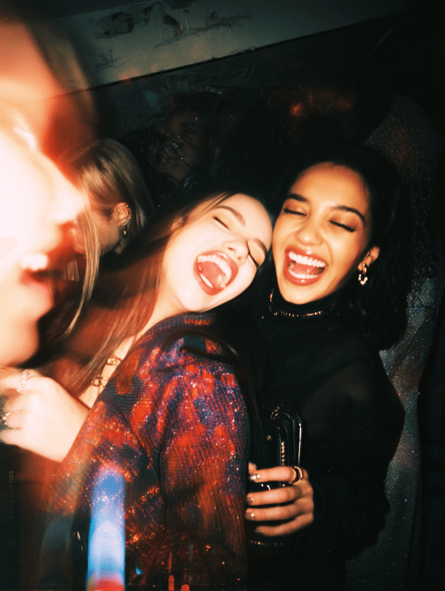 Blurry candid shot of two women laughing and partying in a dark room.