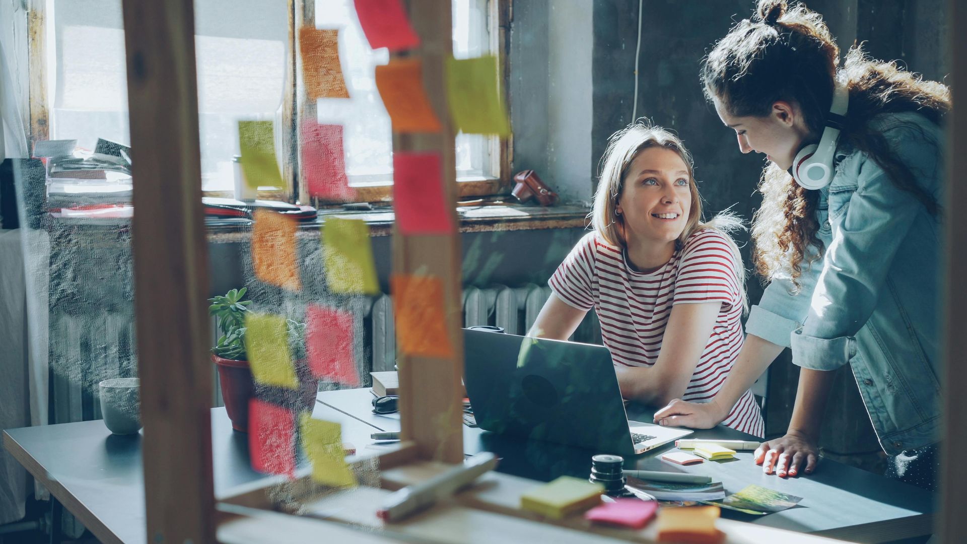 A woman works at her laptop, seen through a glass wall covered in sticky notes
