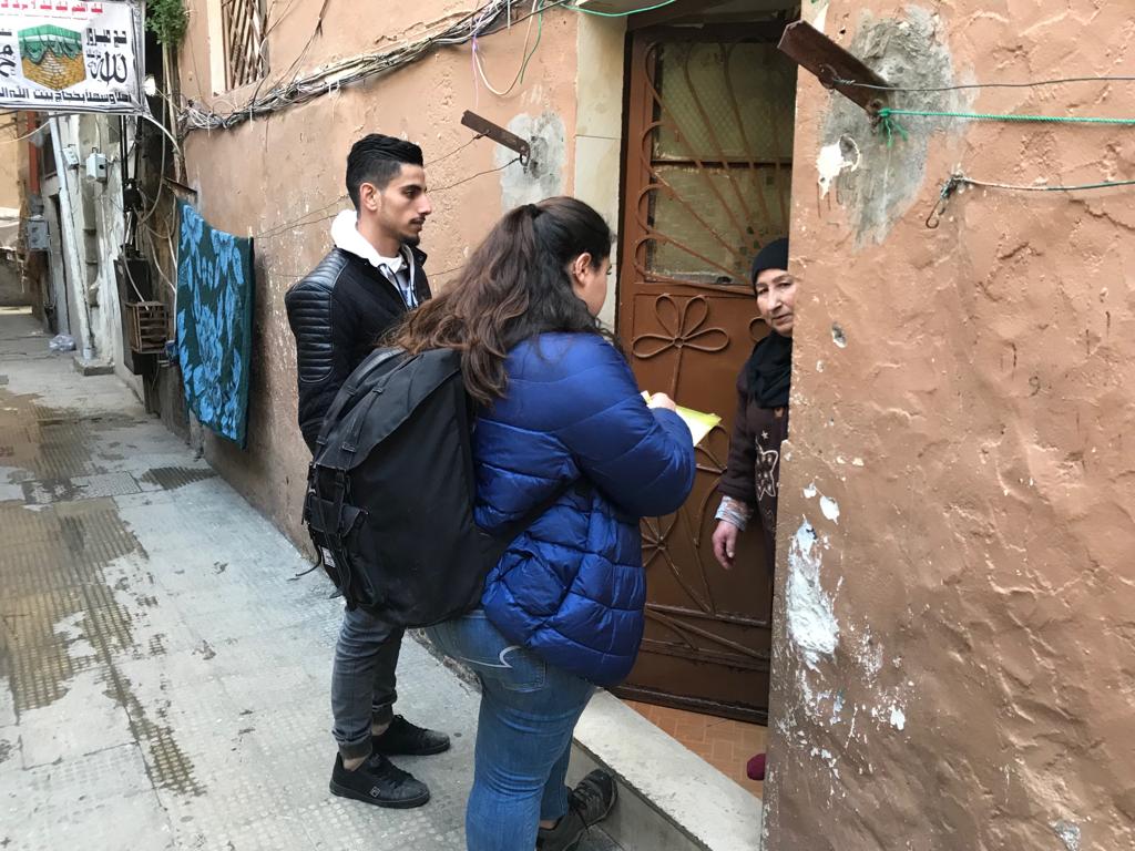 Surveyors speaking to a woman at a door during a survey of Tripoli examining statelessness