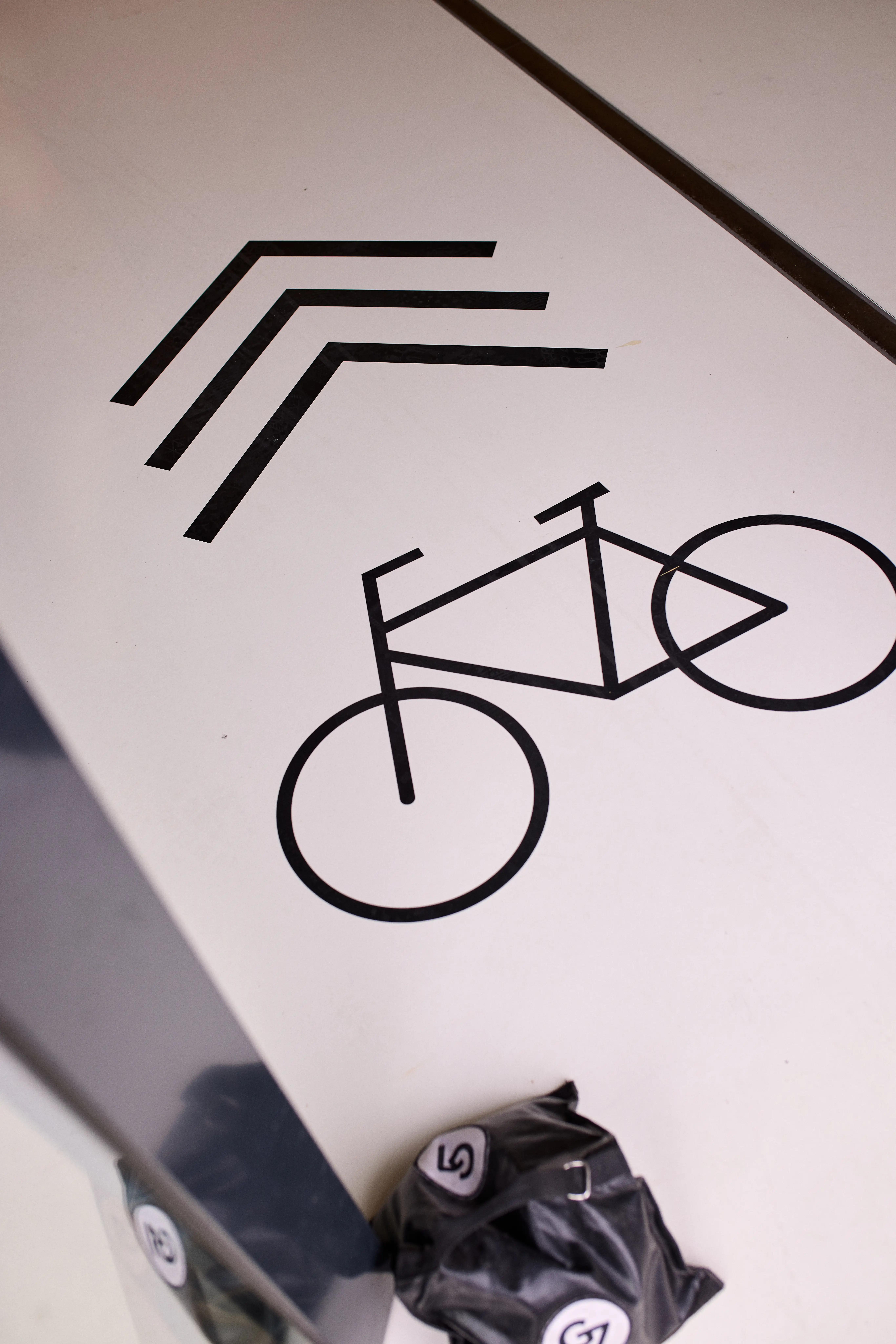 Graphic floor detail at the AGU showcase with black bicycle pictogram and chevron arrows on a white surface.