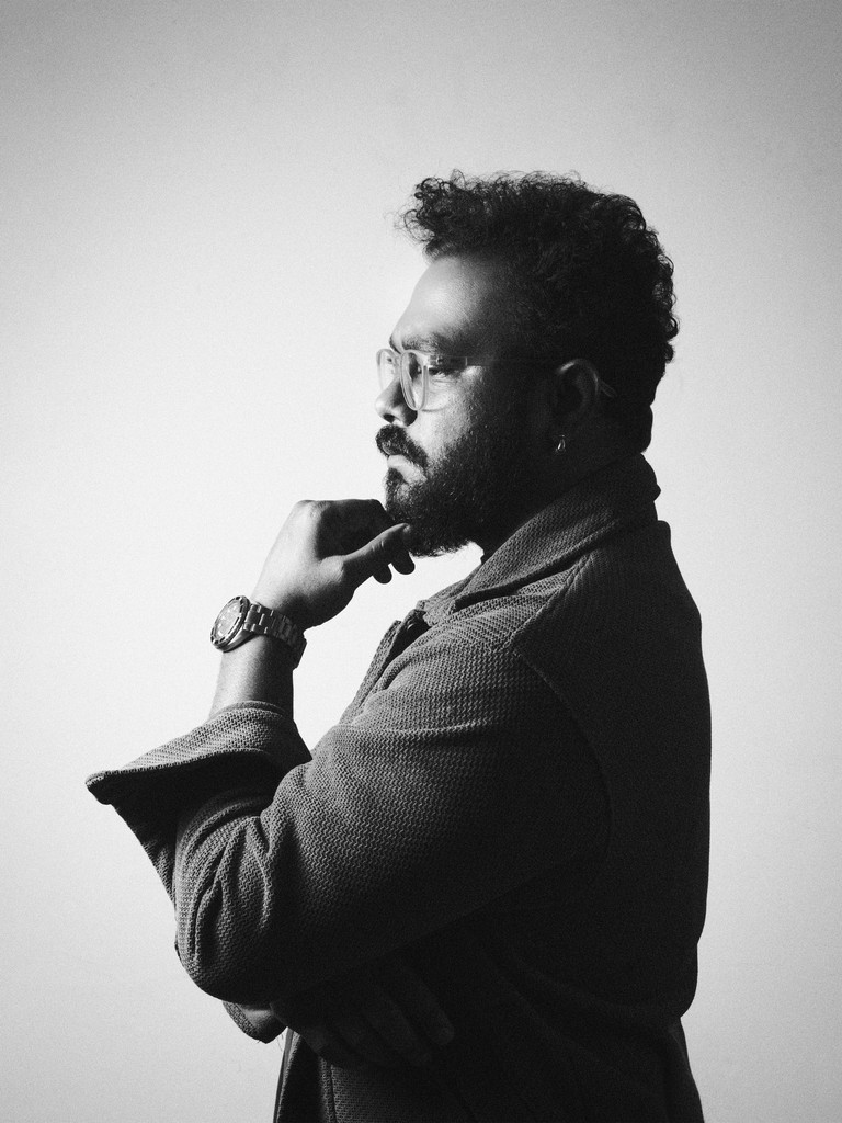 A thoughtful young person with dark hair gazes to the side, captured in soft black and white lighting.