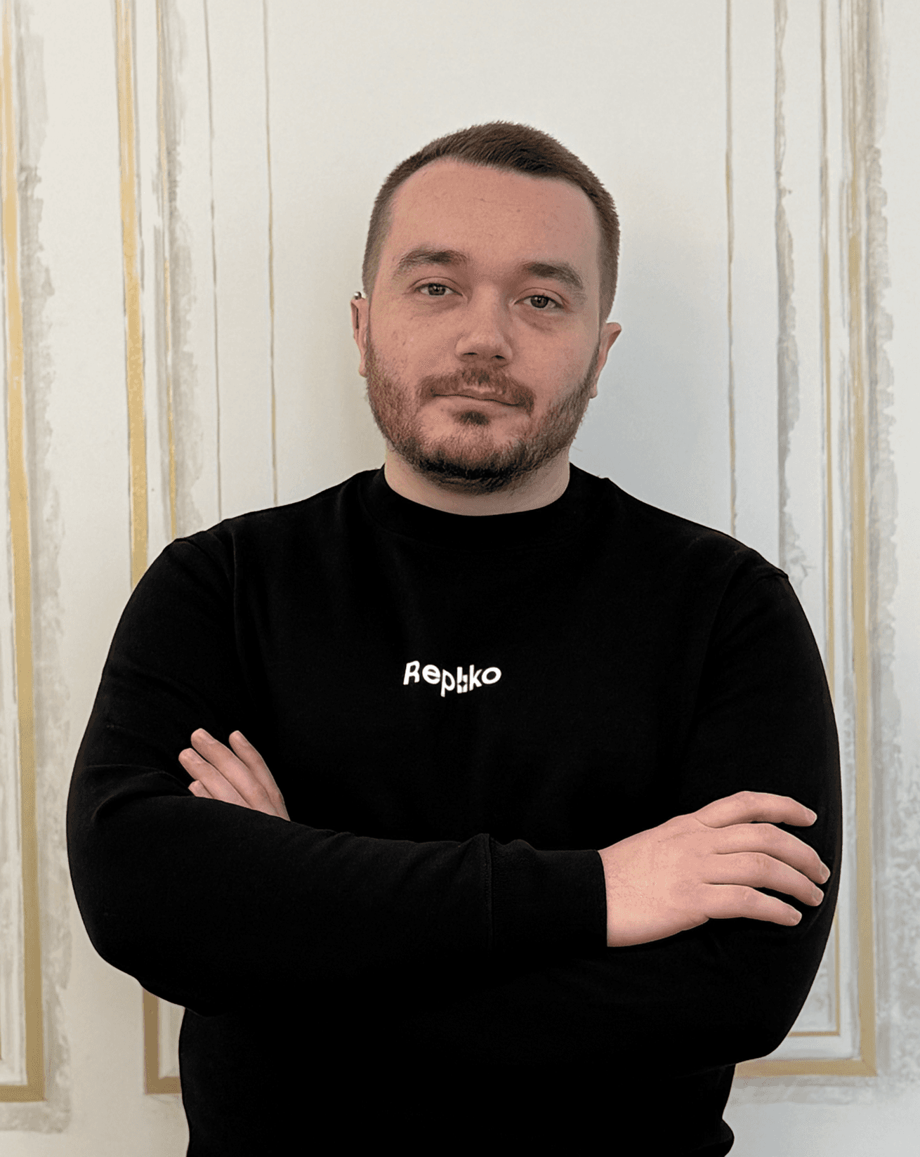 Smiling person with curly hair, wearing a black shirt, against a warm, dark background.