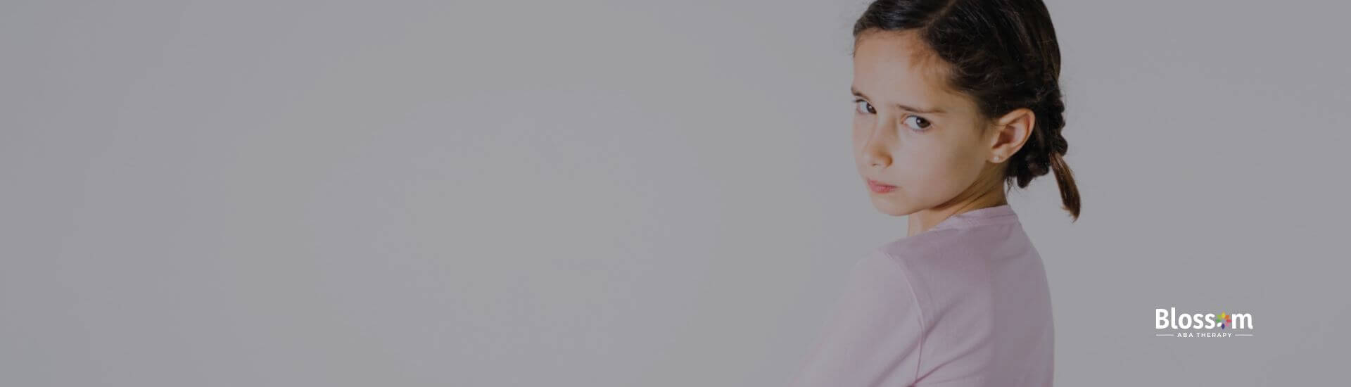 An autistic girl with braided hair, looking upset and standing with her arms crossed.