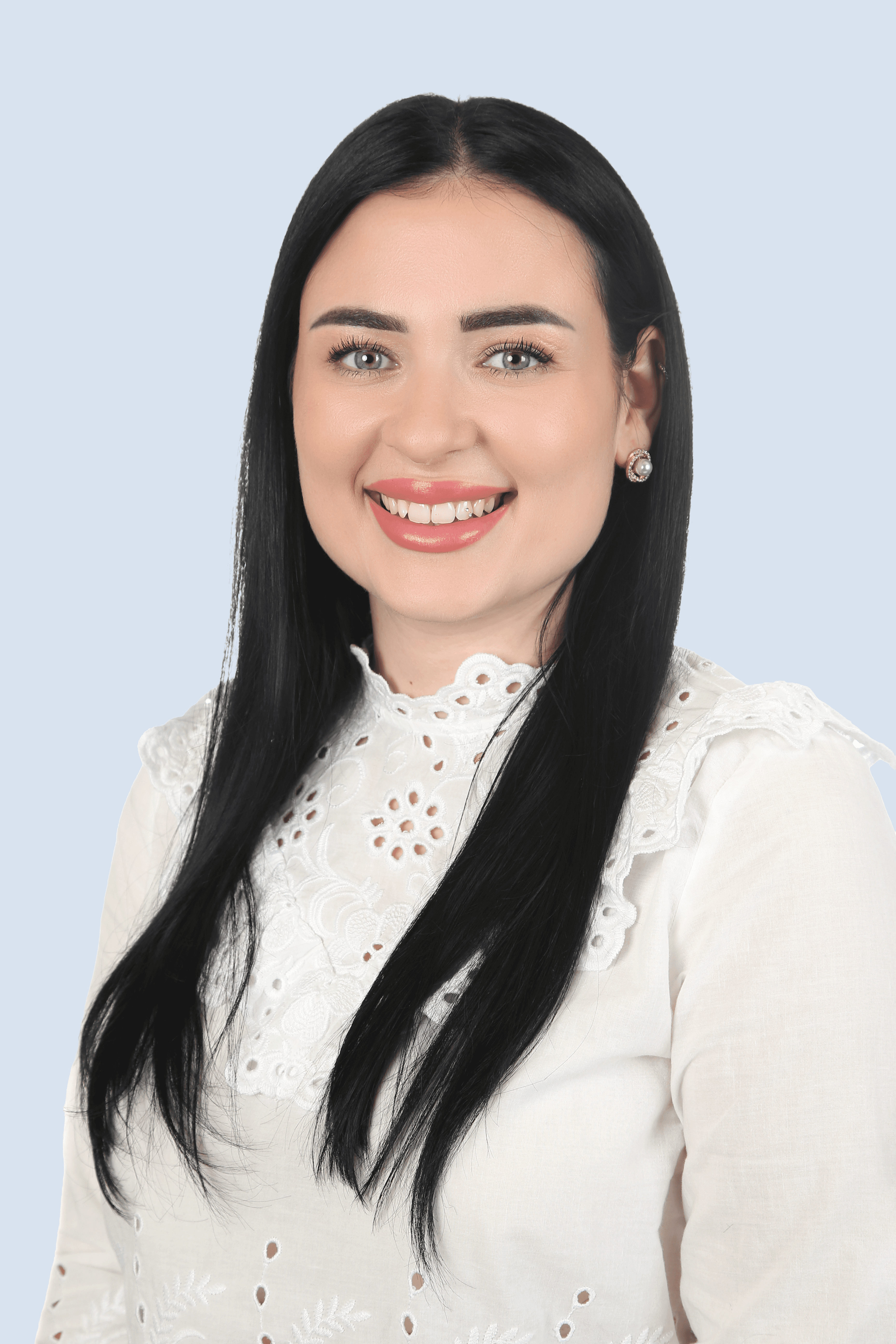 Frau mit braunem Anzug, blauem Hemd und Brille schaut mit verschränkten Armen seitlich in die Kamera und lächelt. 