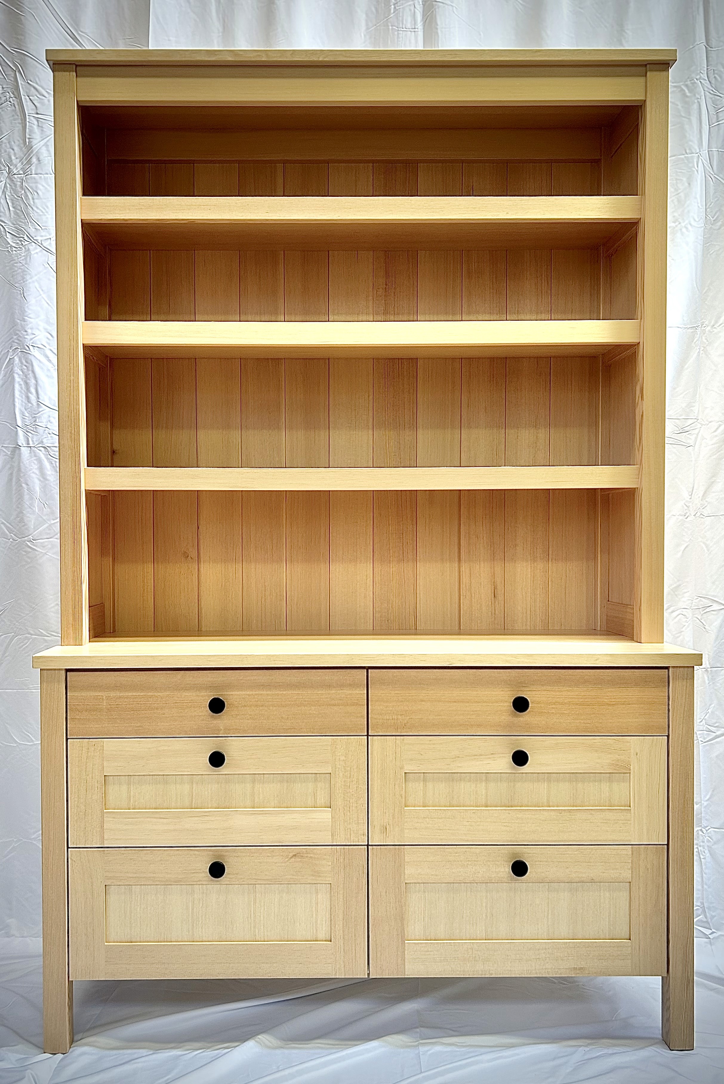 Light wood buffet cabinet with inset upper shelves and lower drawers with dark pull knobs.