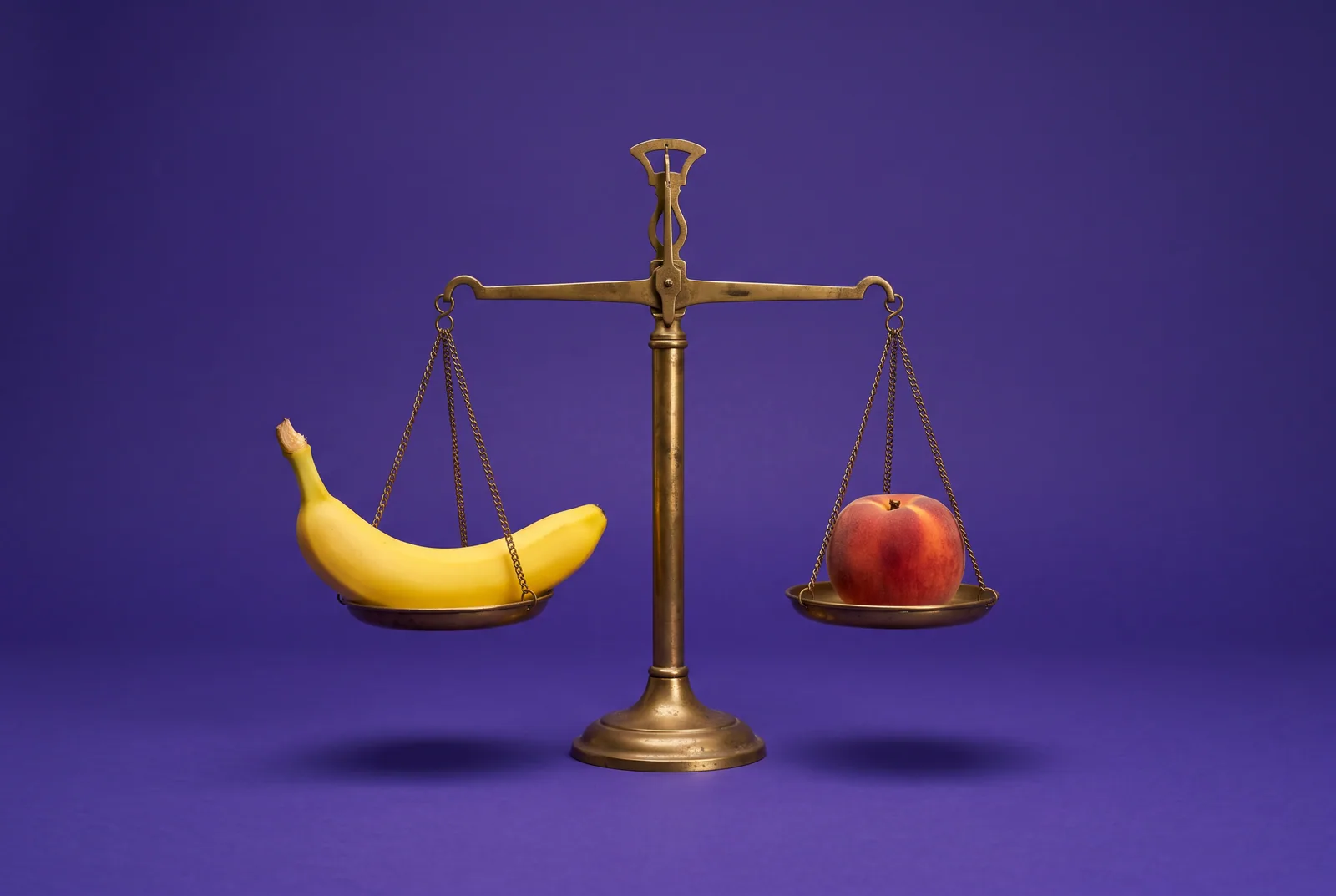 Banana and peach balanced on a brass scale on a violet backdrop, representing deal-breakers and negotiables when your boyfriend watches porn