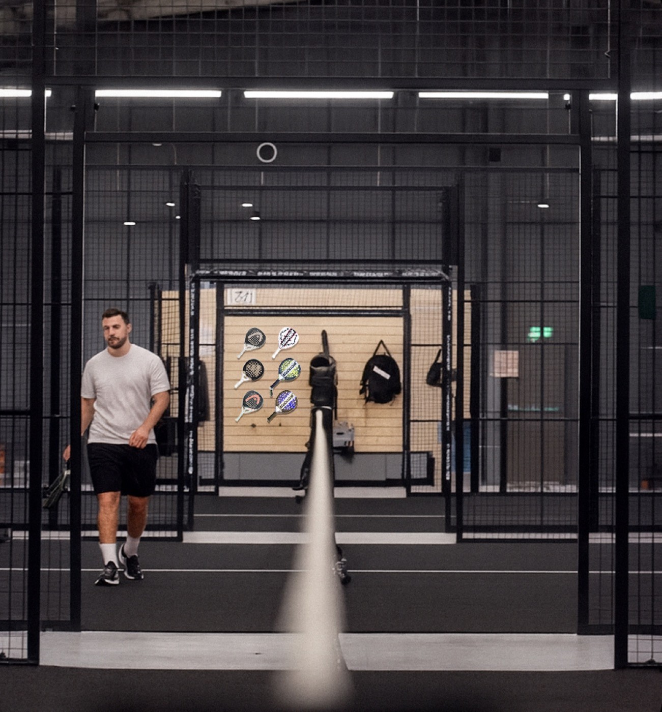 Padelspieler verlässt den Court, im Hintergrund hängen Schläger und Taschen an der Wand – moderner Innenraum und stilvolle Atmosphäre bei Padelnero.