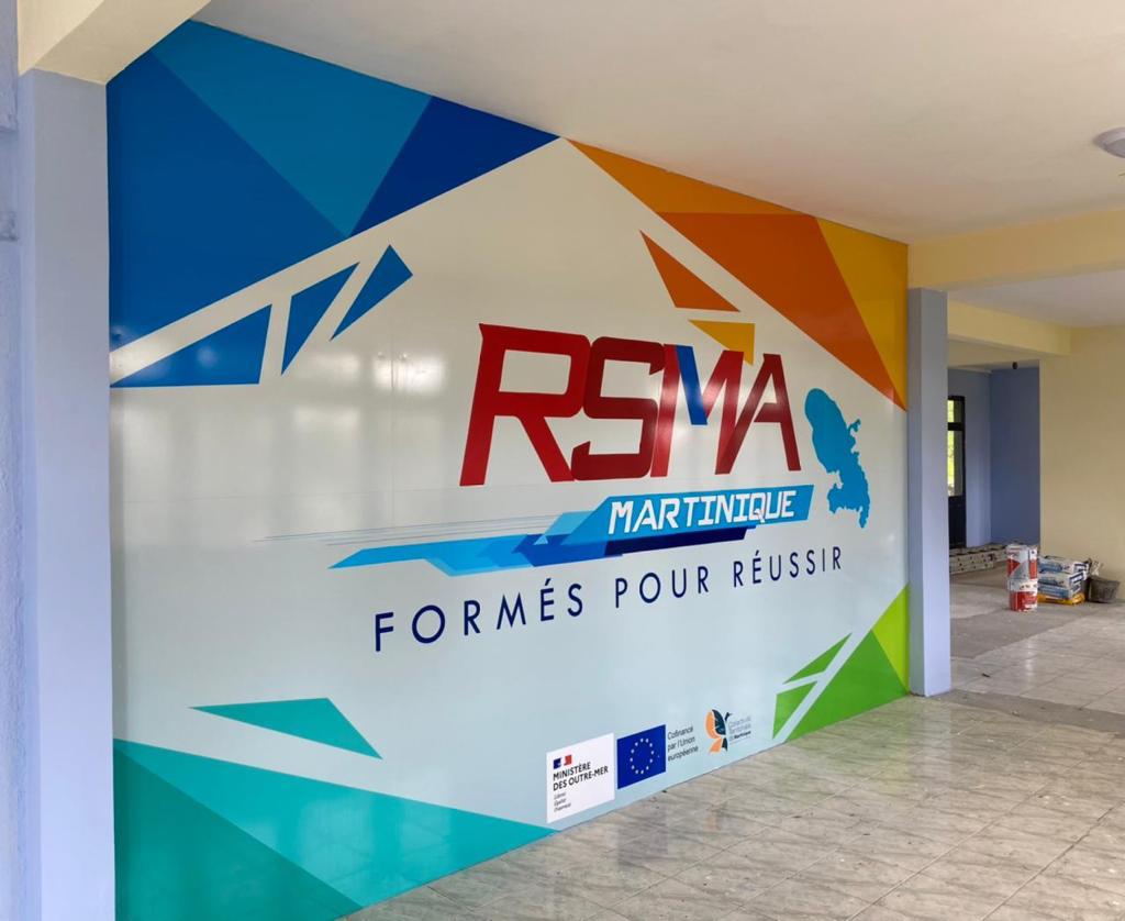 Enseigne colorée représentant « RSMA Martinique » avec une silhouette bleue de la Martinique. Le slogan « Formés pour réussir » est inscrit. Les logos des organisations partenaires sont également présents.
