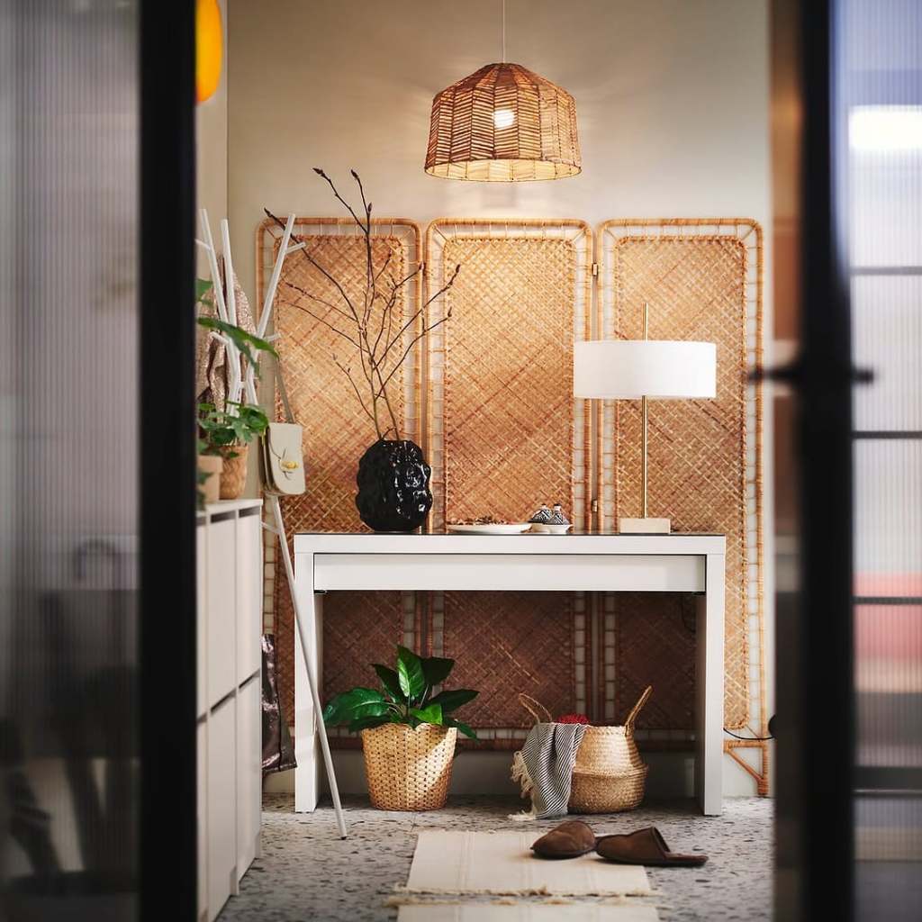 A modern Scandinavian-inspired interior featuring a white table, decorative items, plants in woven baskets, and a stylish hanging lamp, set against a textured backdrop with a natural theme.