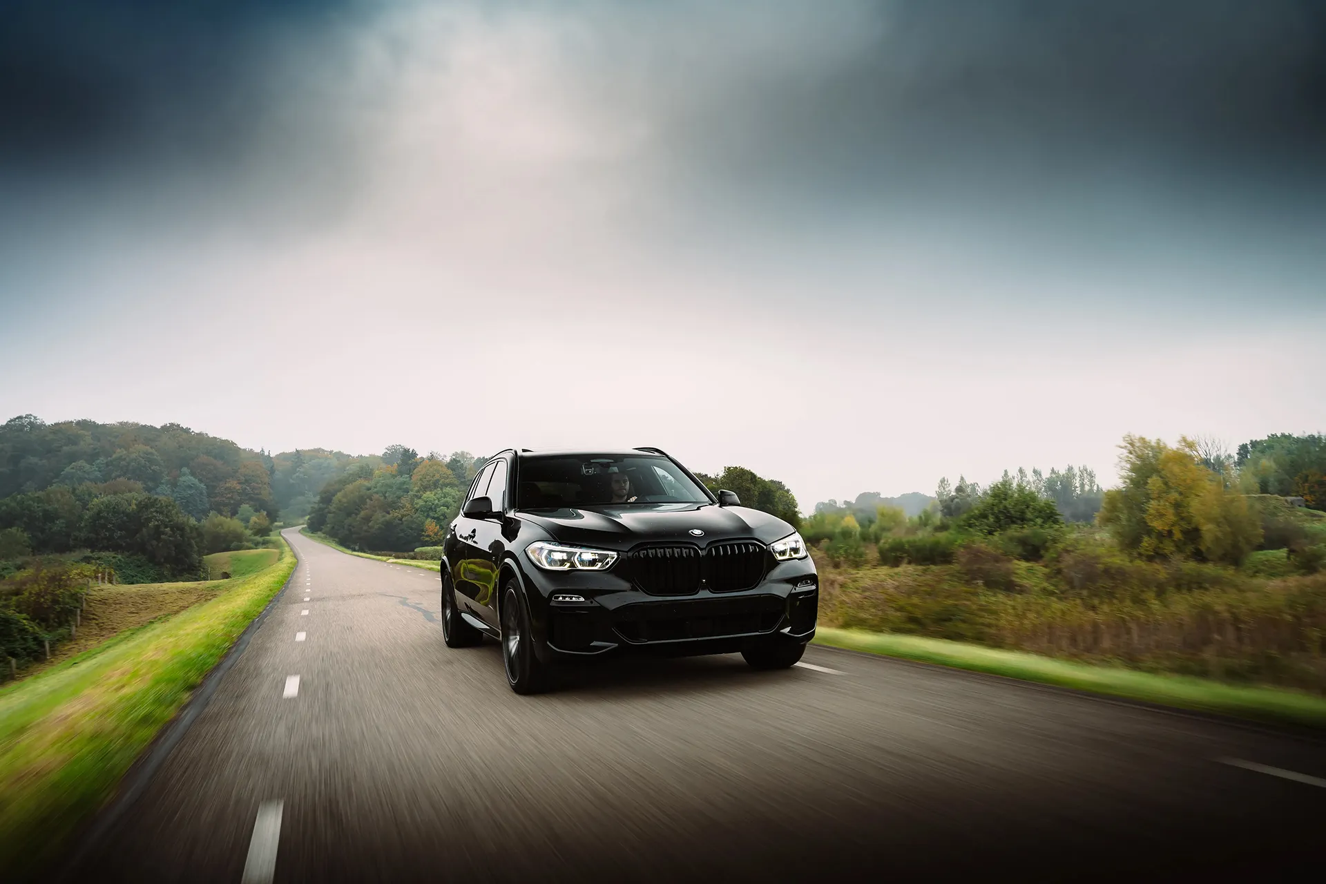 Cinematic frontside image of a BMW riding on a road with a flat green nature environment