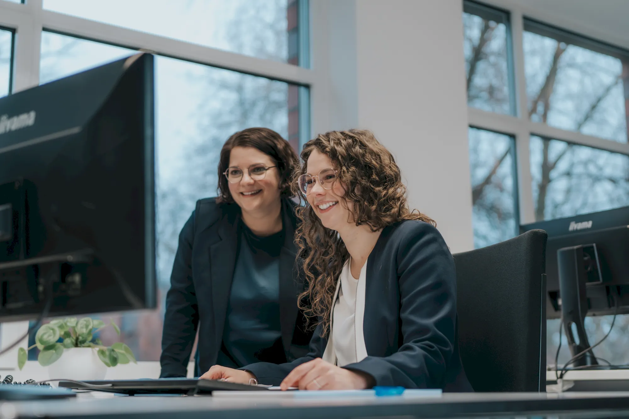 Zwei lächelnde Frauen im Büro arbeiten an Computern. Teamwork und Büroalltag.