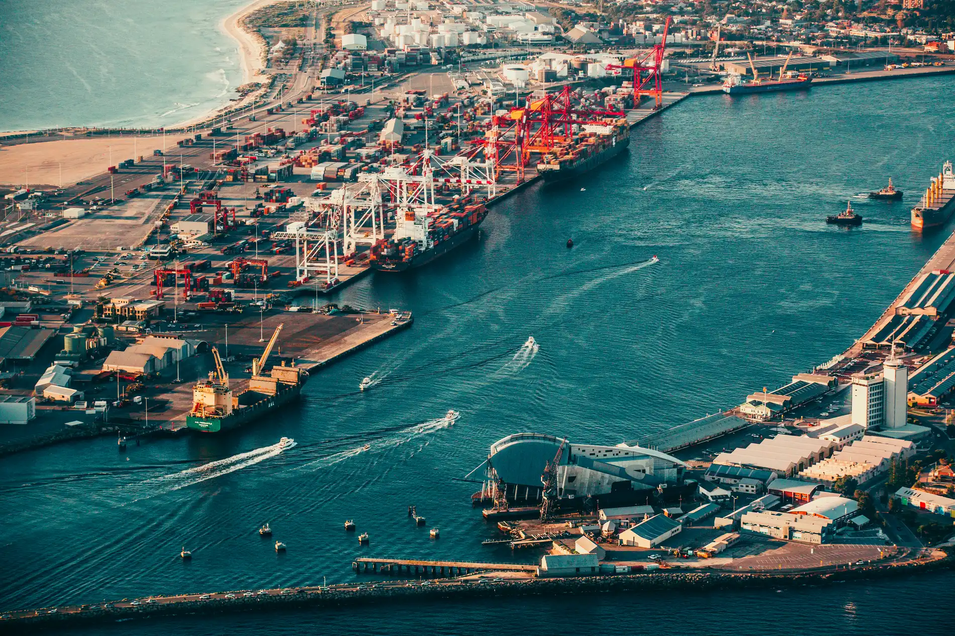Aerial of a working port at golden hour, cranes and container yards beside a boat channel