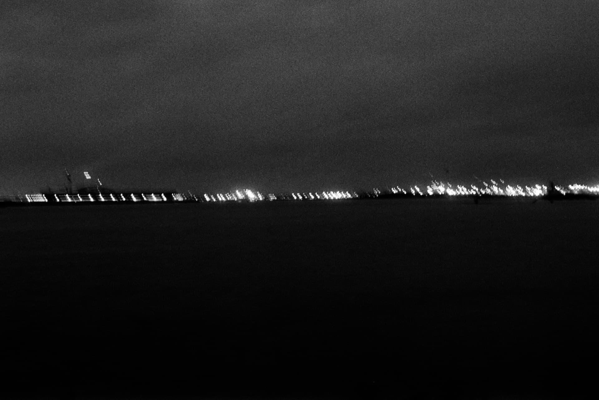 Distant lights along far shore of Thames at night with dark water in foreground
