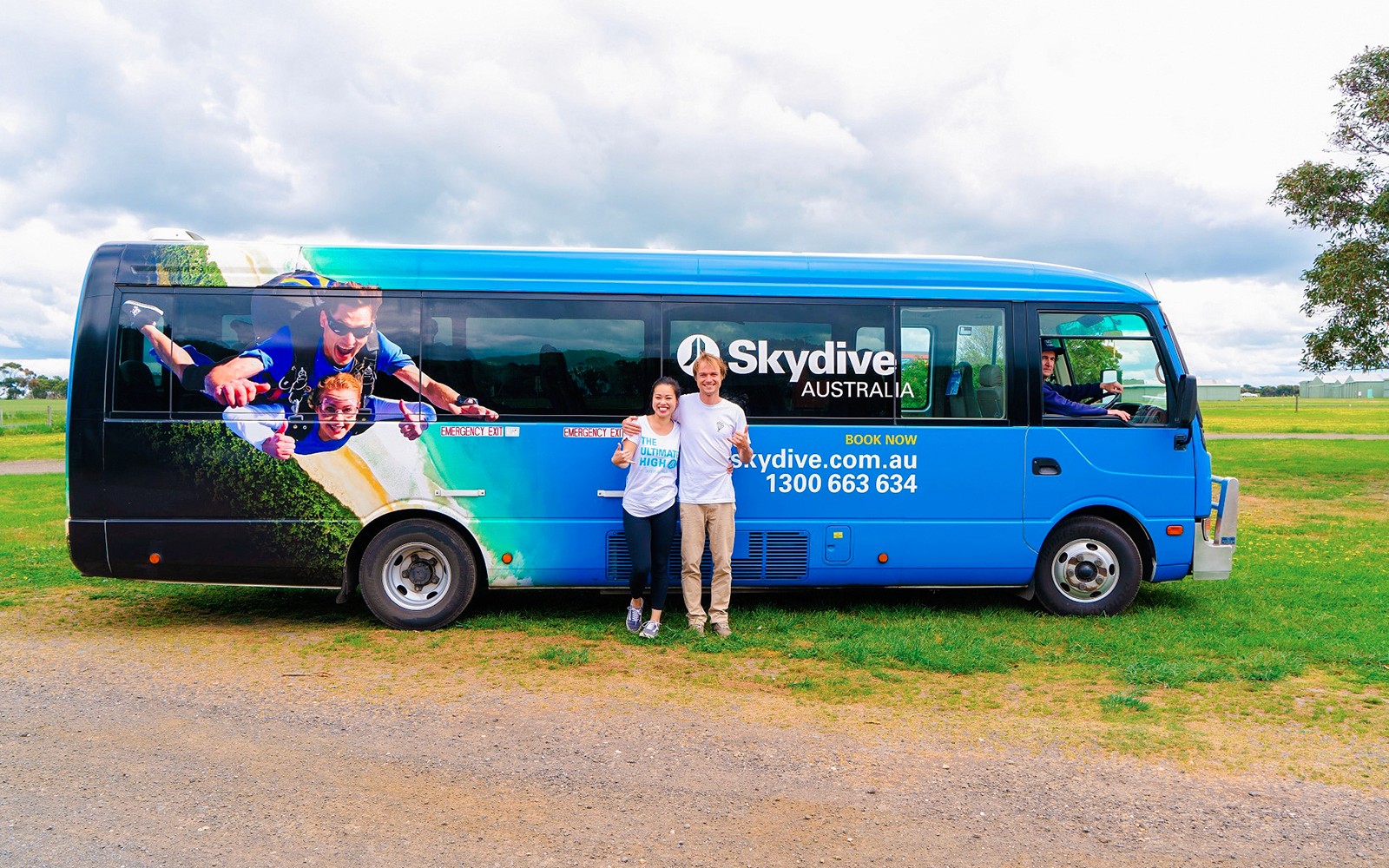 אוטובוס Skydive Airlie Beach עם גרפיקה של צניחה ועם שני אנשים עומדים לצדו.