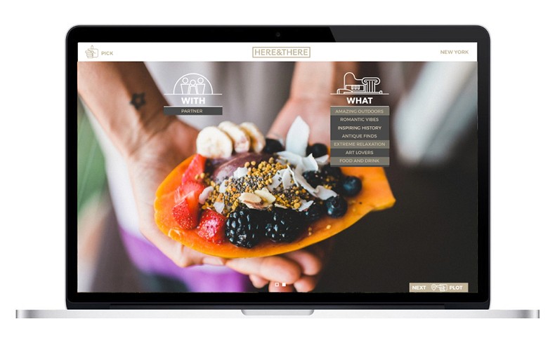 A laptop screen displays a food website called "HERE&THERE." The website features a clean, minimalist design with a white background and black text. The navigation bar includes options like "WHAT," "AMAZING OUTDOORS," "ROMANTIC VIBES," "INSPIRING HISTORY," "ANTIQUE FINDS," "EXTREME RELAXATION," "ART LOVERS," "FOOD AND DRINK," "NEXT," "PLOT," and a "PICK" button. A central image shows a person holding a yellow plate with fruits like strawberries, blackberries, and bananas. The website's logo includes a stylized piano keyboard graphic. The laptop screen is positioned above a silver laptop stand.