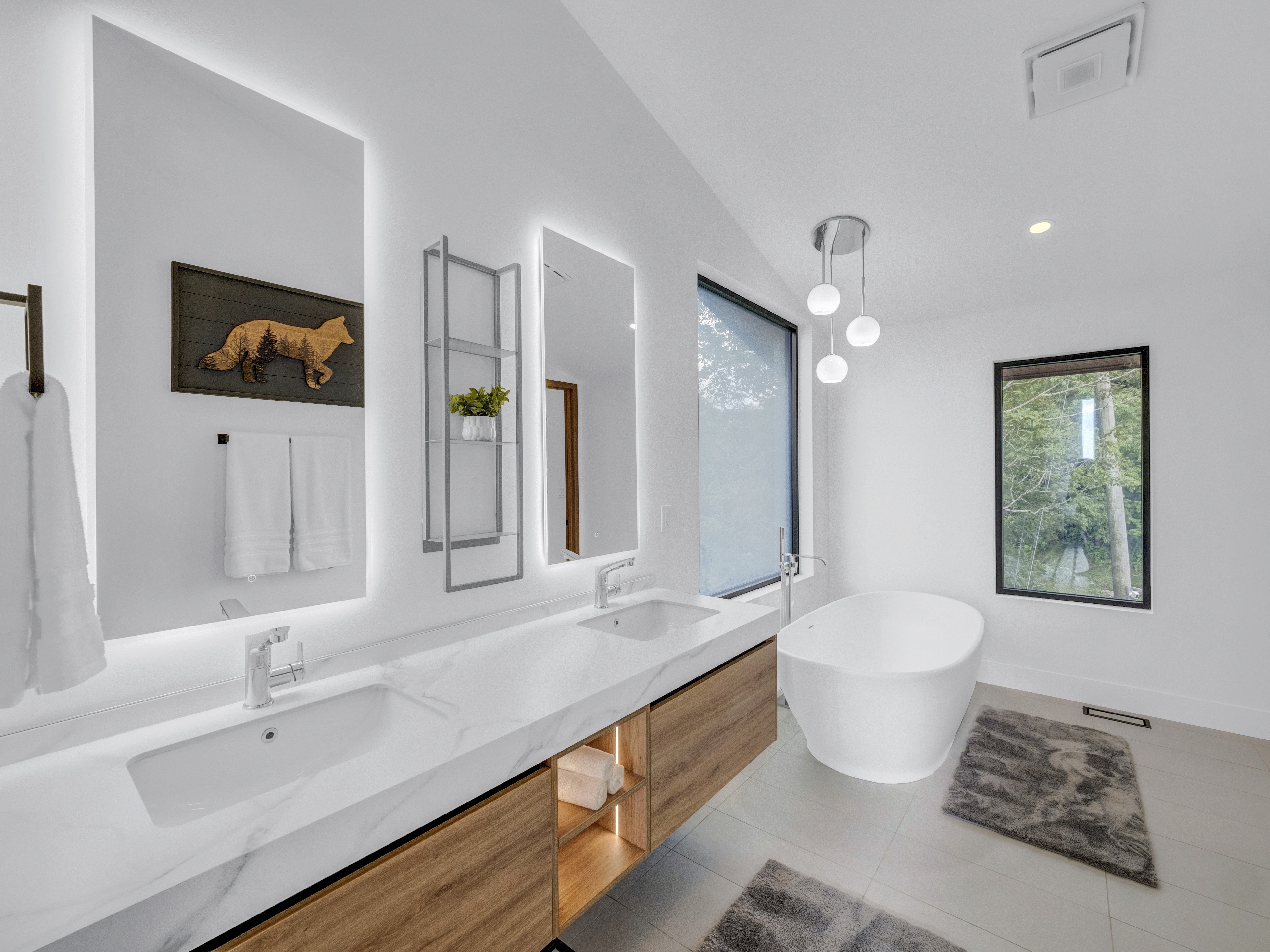 Wide angle of the primary spa bathroom featuring a floating double vanity and a freestanding soaking tub by the window