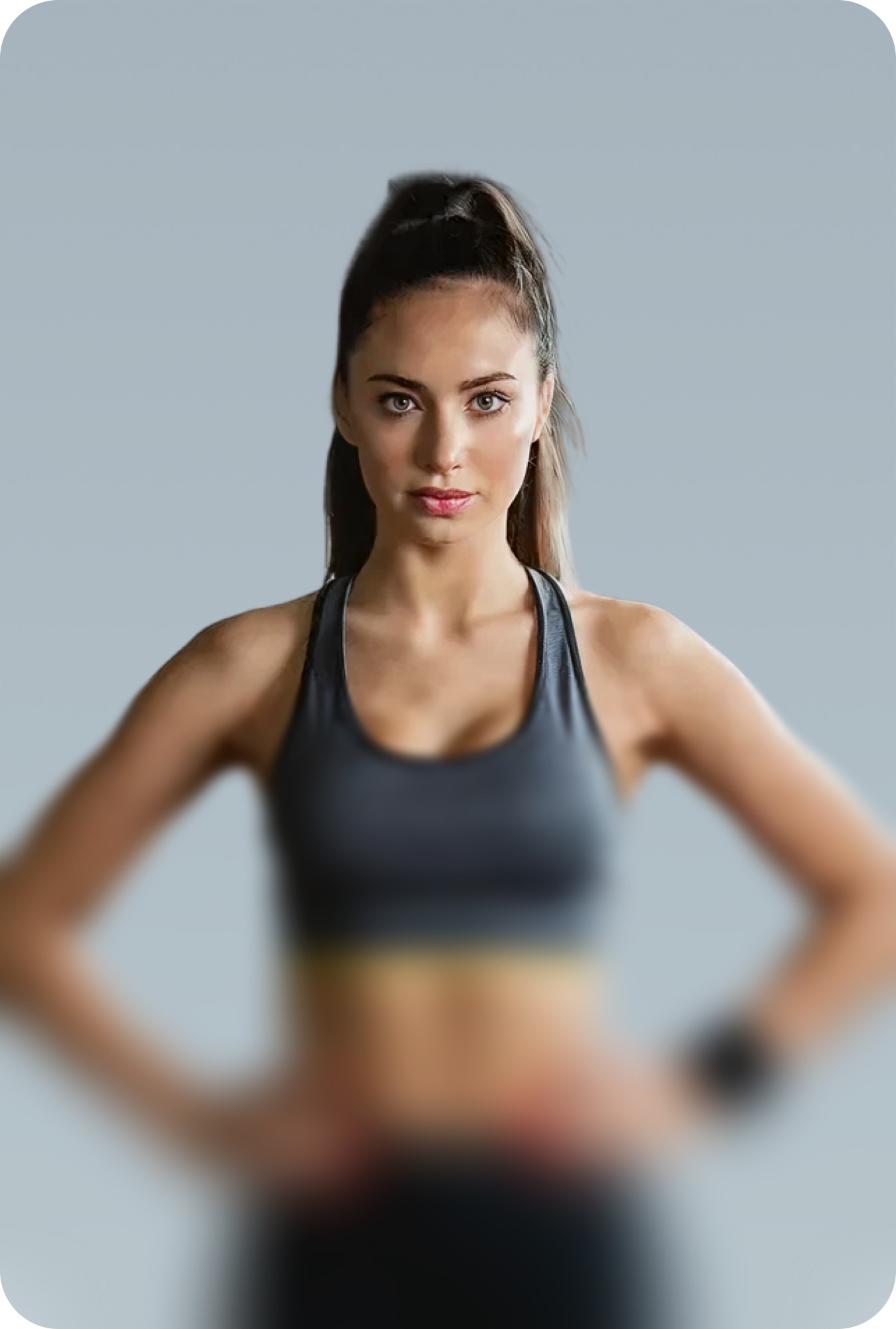 Woman in a sports bra smiling with her hair in a bun on a grey background.