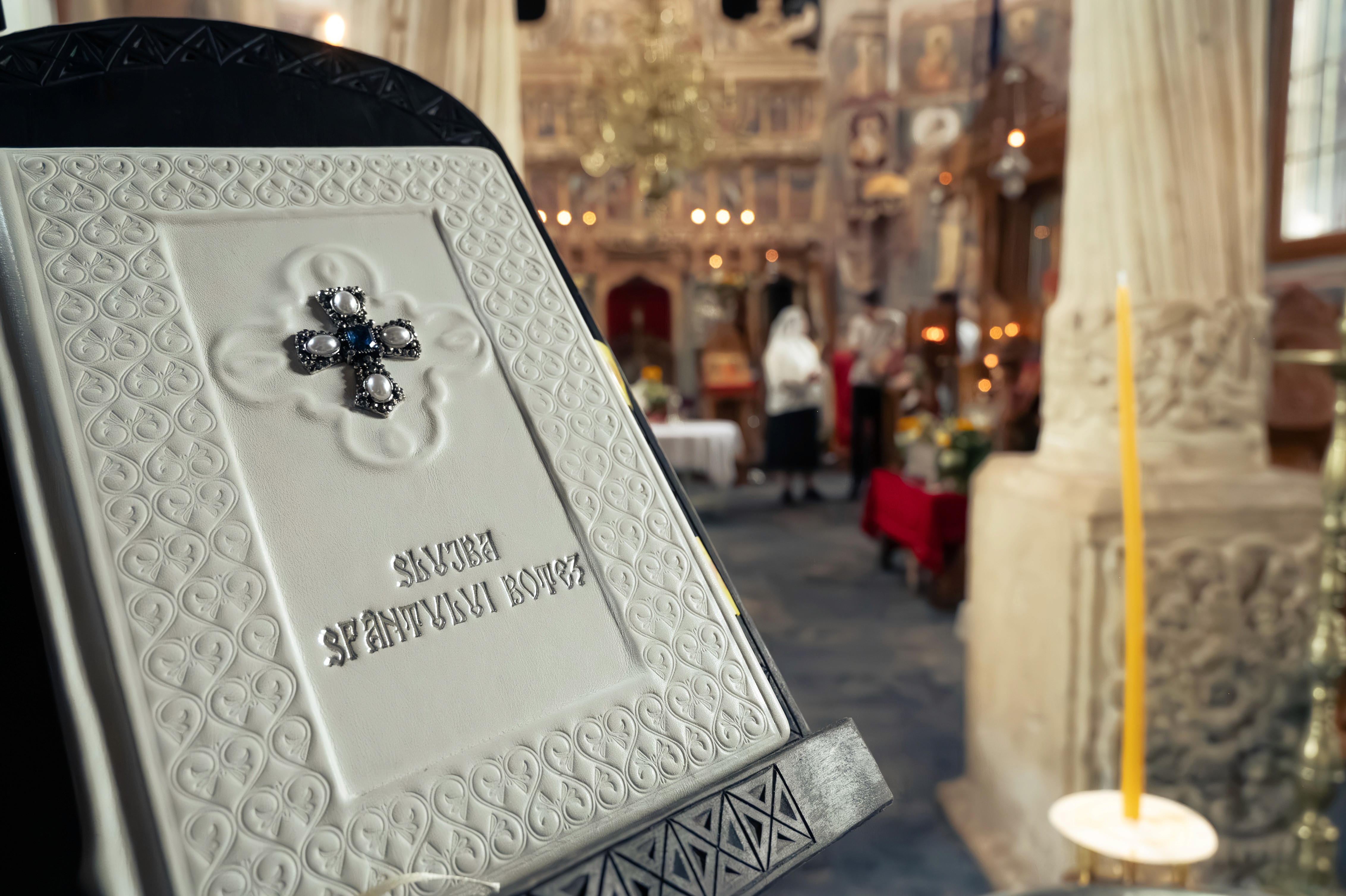 Interiorul bisericii pregătit pentru slujba de botez — cristelniță și aranjamente florale fotografiate profesional.