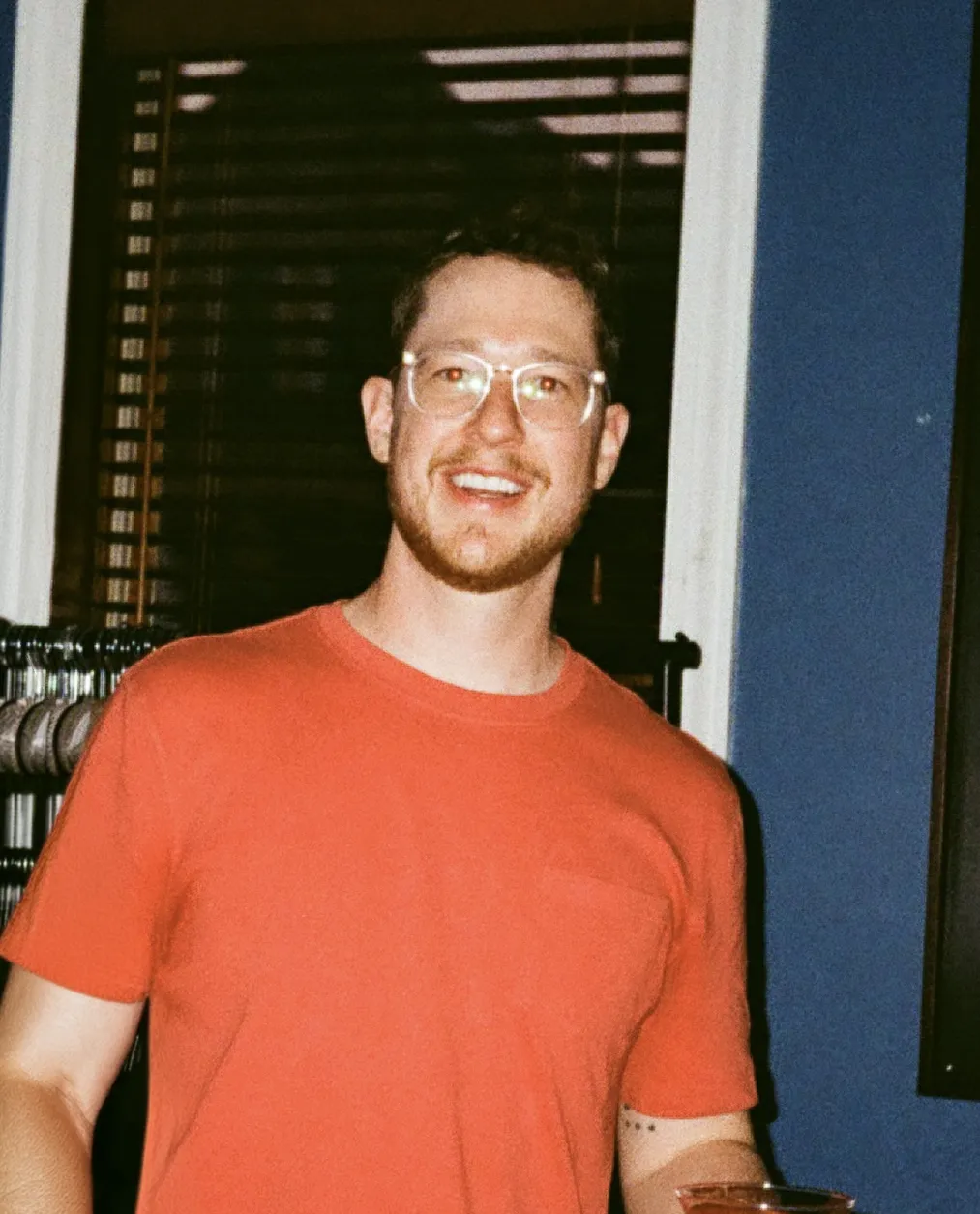 Portrait of a smiling man wearing glasses and a red shirt indoors