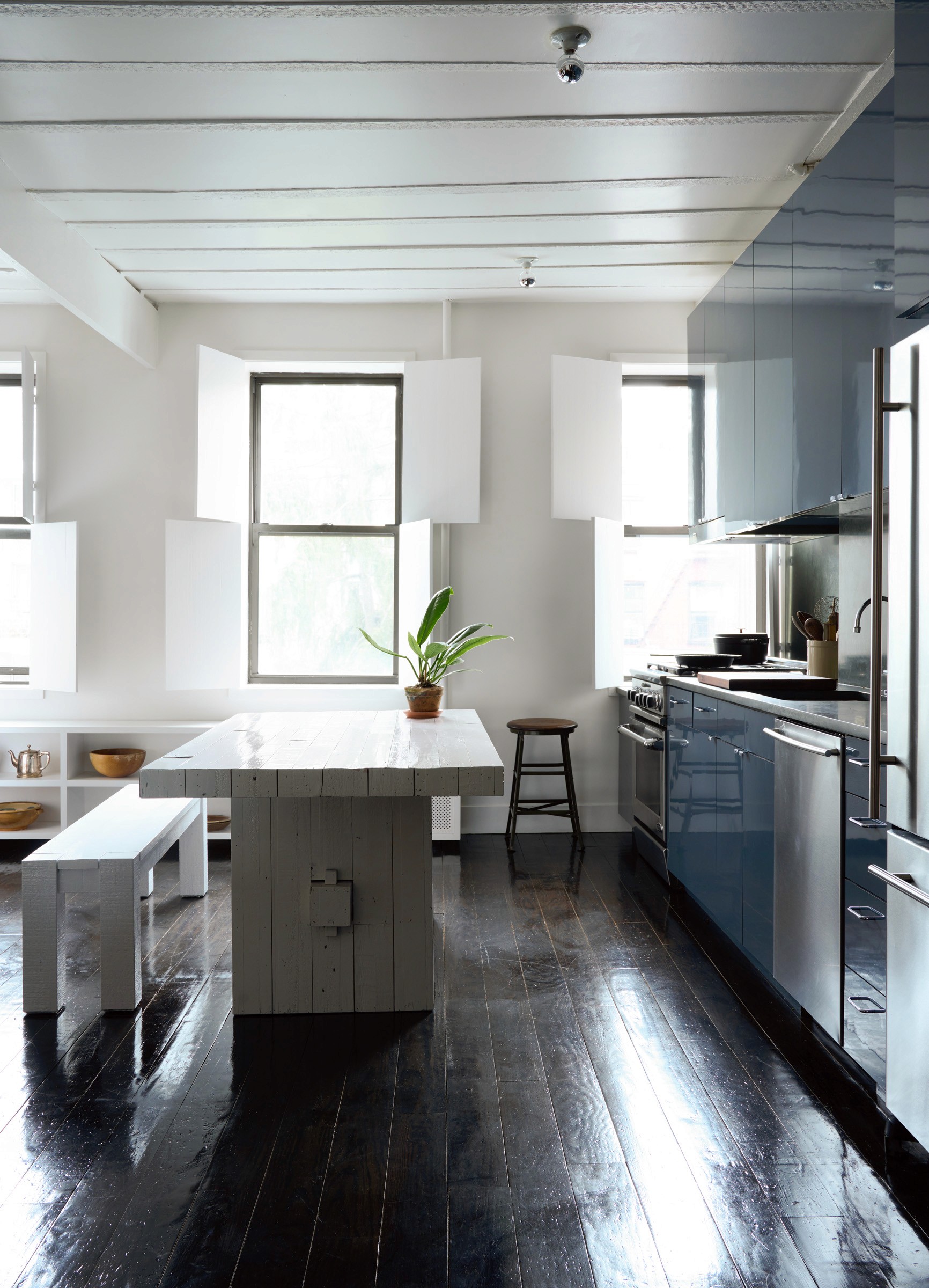Kitchen with blue high-gloss cabinetry, white wooden table, and dark floors.